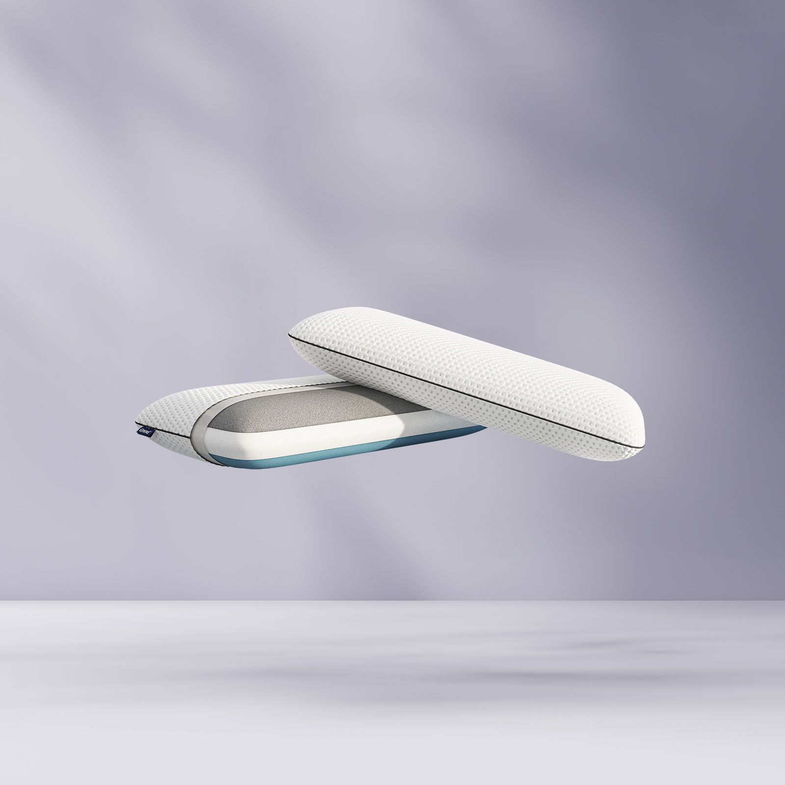 Deux oreillers blancs modernes en mousse à mémoire de forme avec des housses en filet flottant, l'un montré fermé, l'autre ouvert pour révéler les couches de mousse à l'intérieur, sur un fond violet clair et doux.