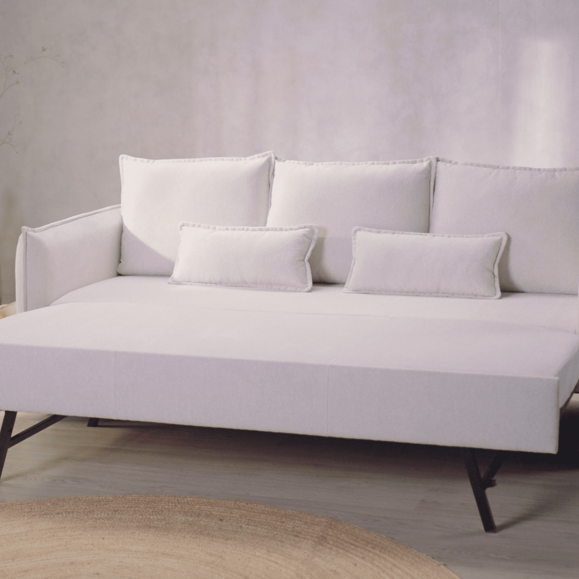 Helles Schlafsofa mit Rücken- und Zierkissen vor grauer Wand