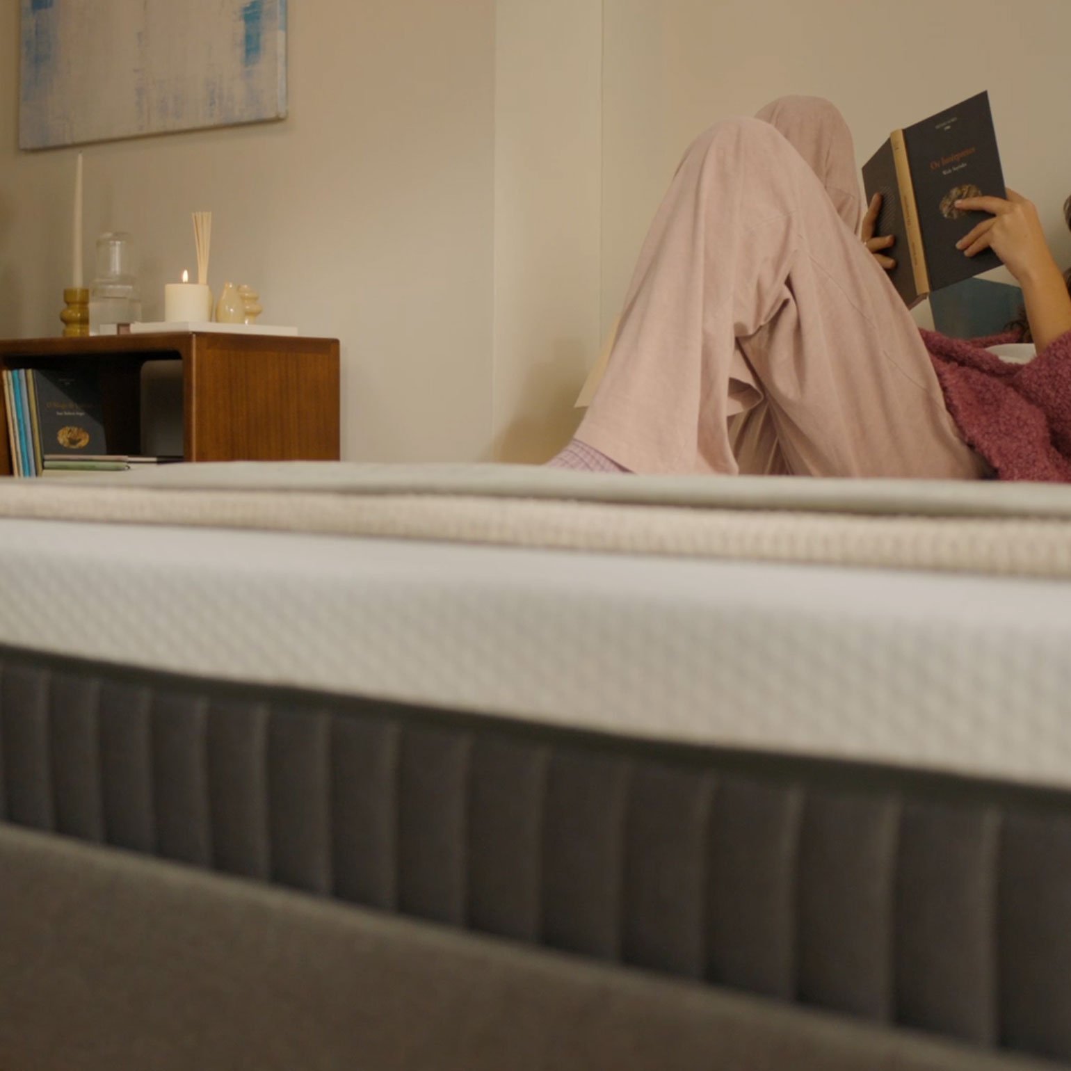 Woman reading a book on an Emma Original Lite mattress in a cosy bedroom, with the mattress in close-up foreground.
