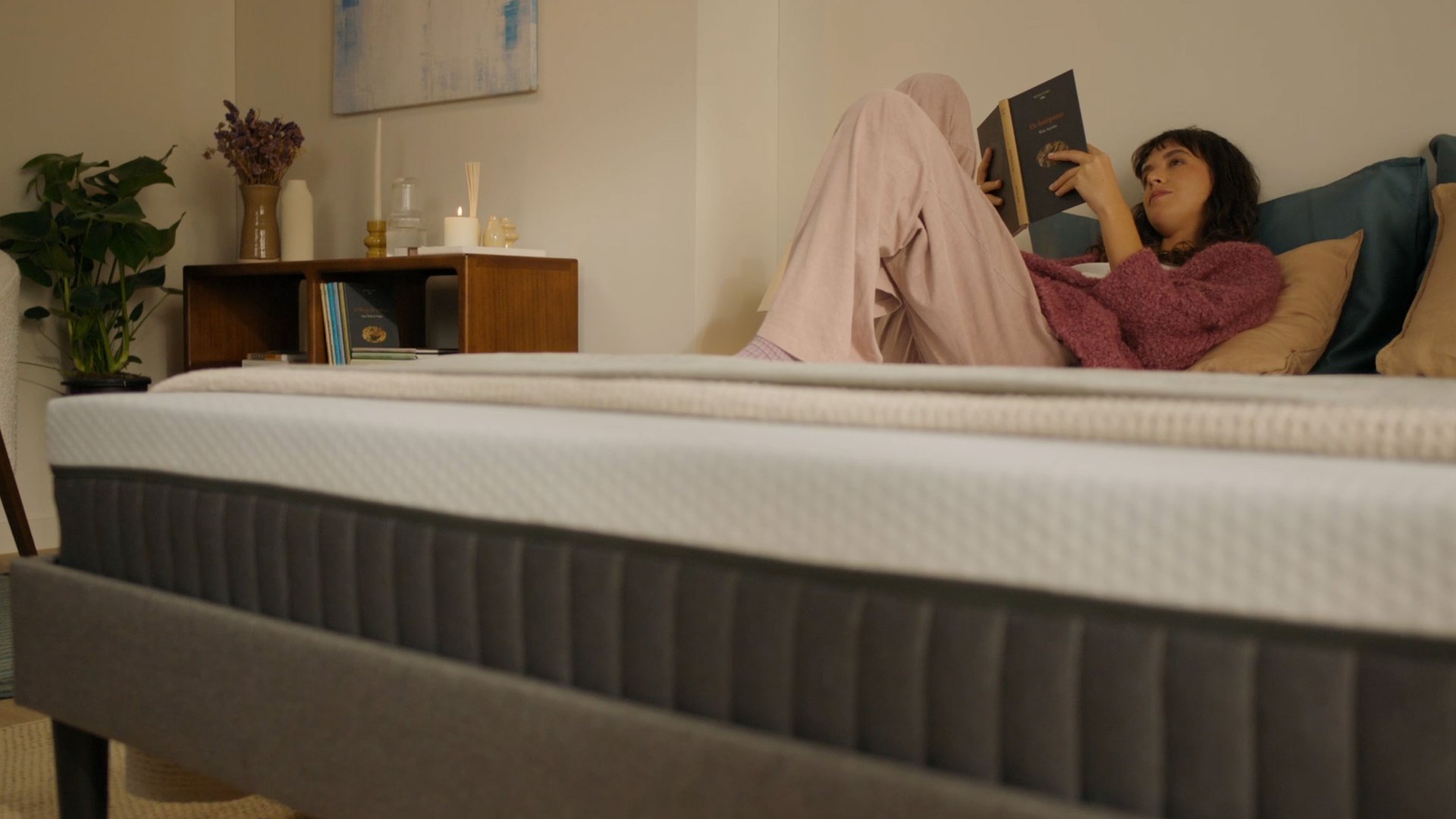Person sitting on a bed with a white mattress in a bright bedroom.
