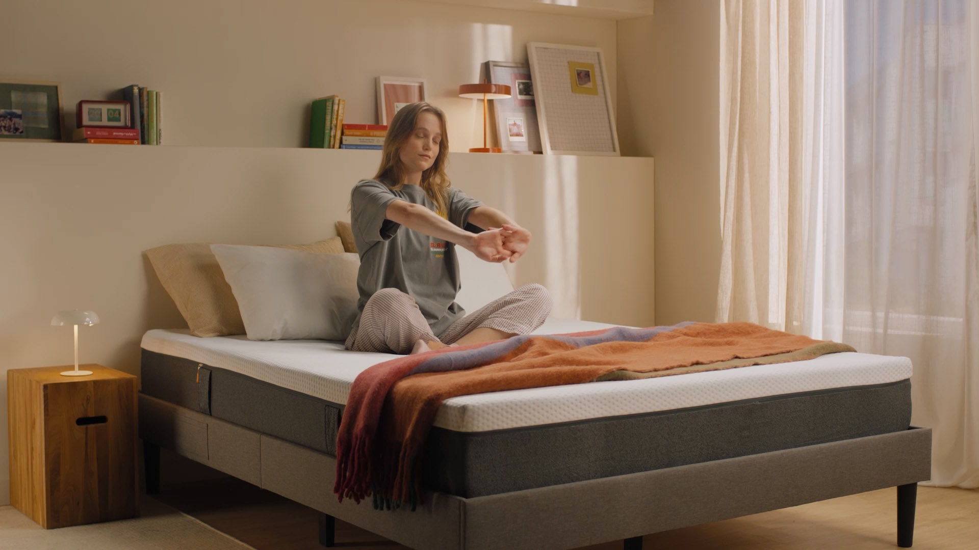 Person sitting up on a bed with a white mattress in the morning.