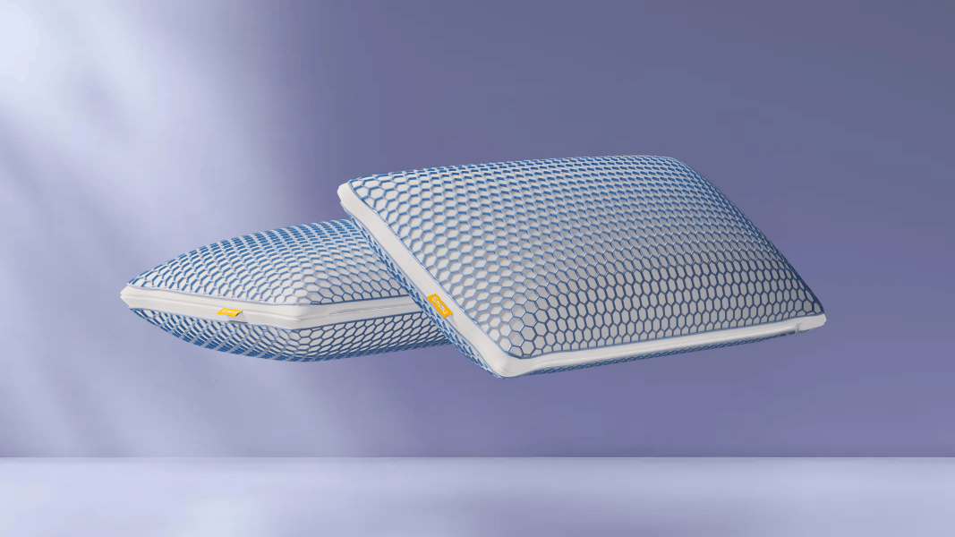 Twee witteAirGrid® Adapt Kussens met blauw-wit hexagonaal raster zweven tegen lichtpaarse achtergrond; gele merklabels zichtbaar aan zijkant, benadrukt luchtige structuur en setverpakking.