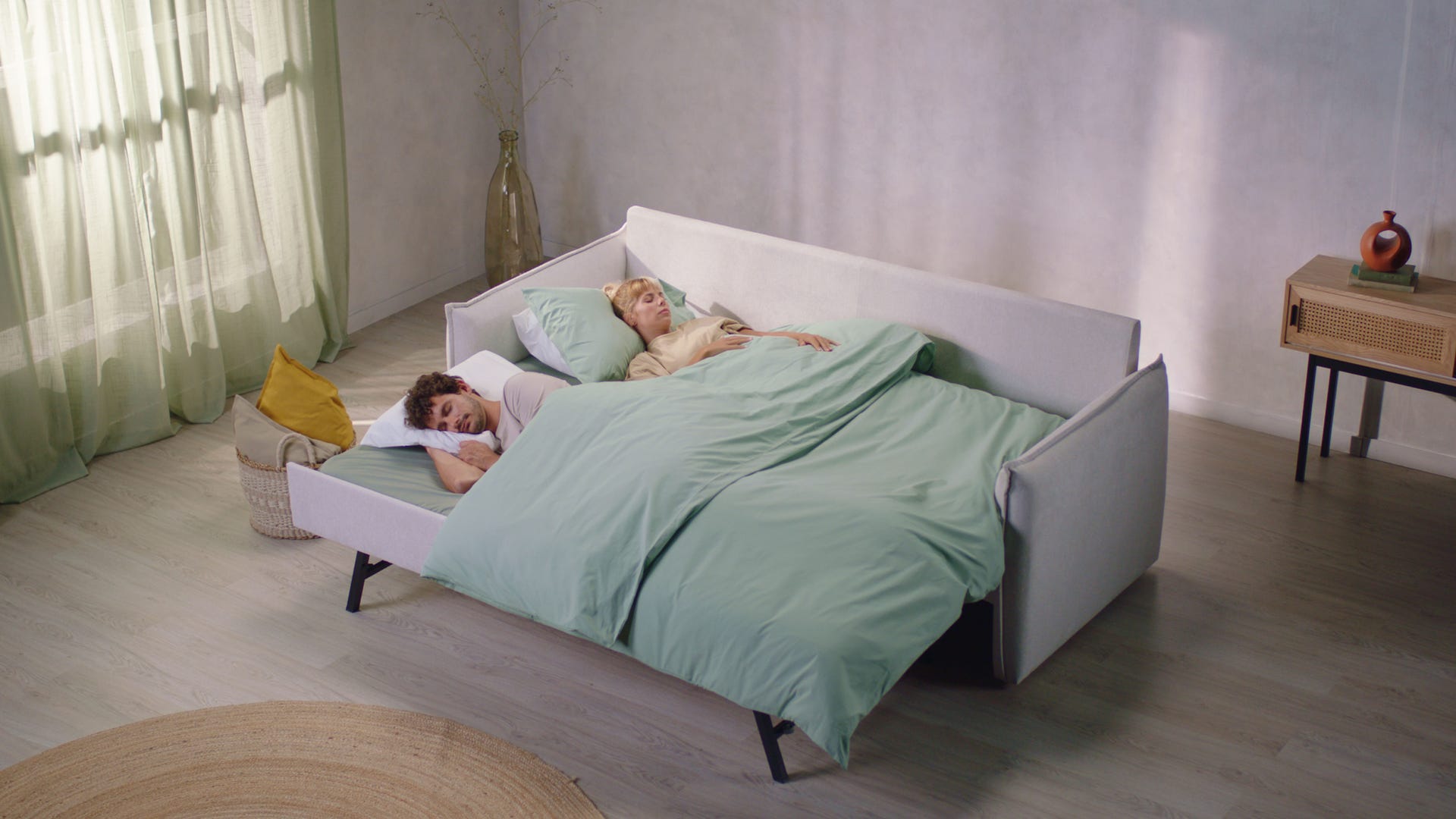 Sofa cvama convertible en una cama doble grande donde duerme una pareja con sabanas verdes