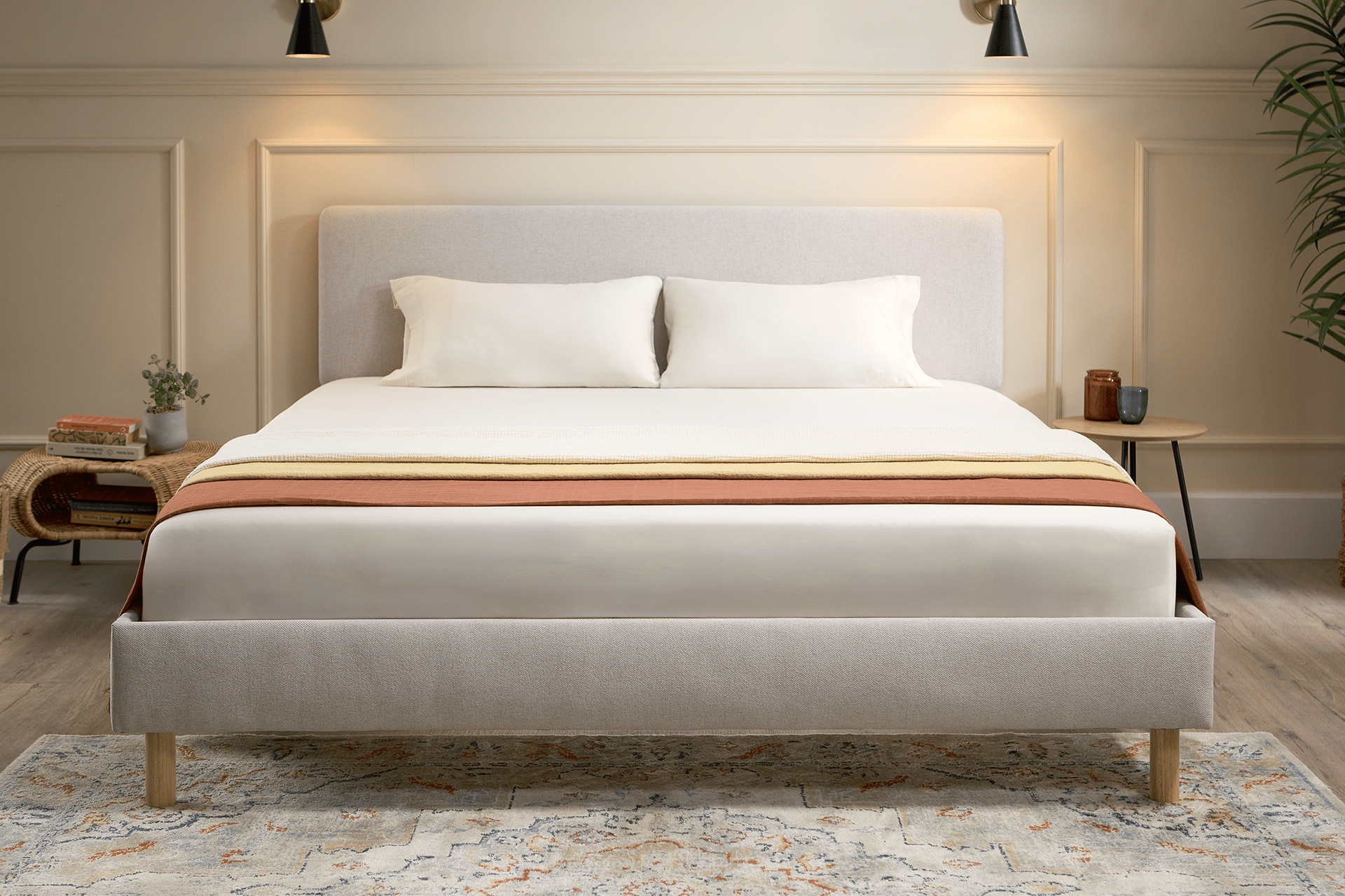 Emma Boxbed in beige with upholstered headboard and wooden legs, styled in a warm Scandinavian bedroom.