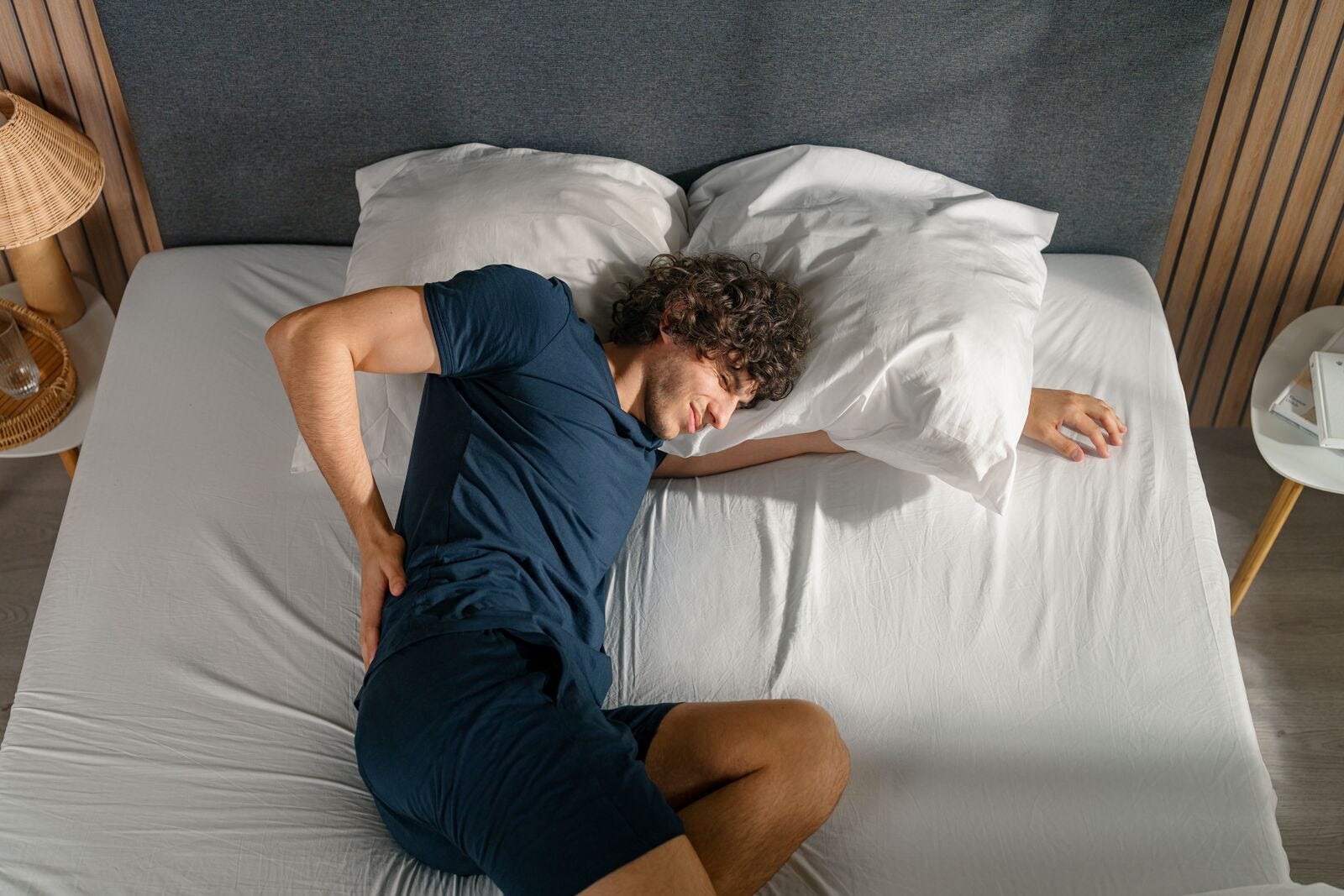 Persona joven en pijama azul tiene problemas de espalda al dormir en su cama