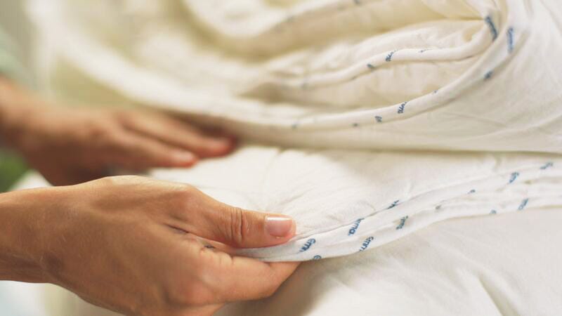 Main d’une personne pliant une couette blanche Emma, avec texte bleu imprimé sur le tissu. La texture douce et les plis visibles mettent en valeur la qualité et la souplesse du matériau. L’image suggère une couette fraîchement lavée ou neuve.