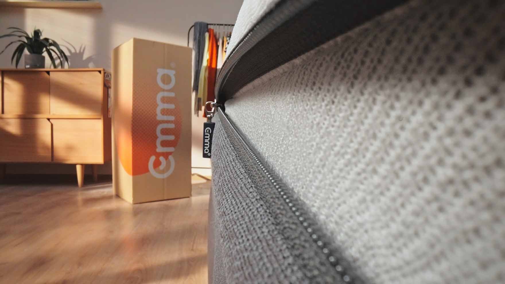 Close-up of a zipper with the label "Emma" on it. On the side, there is an "Emma" cardboard with an orange design