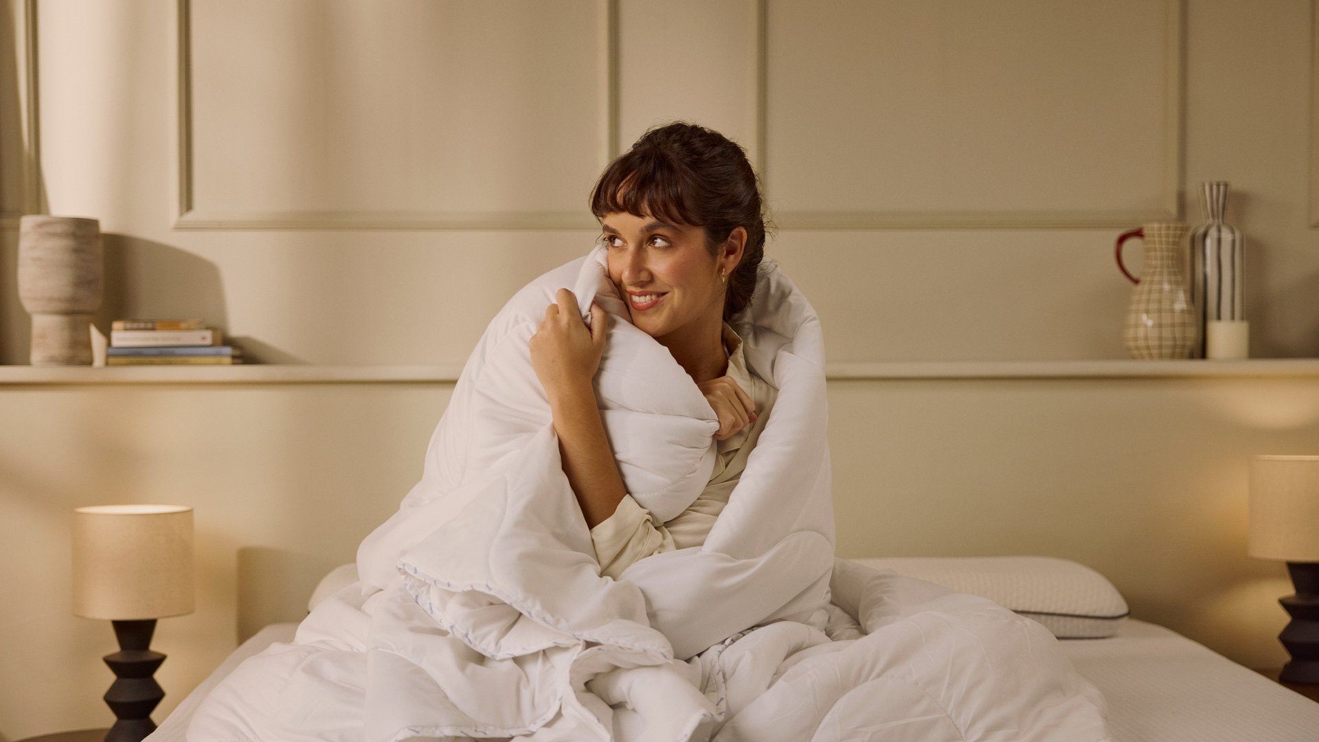 Imagem de uma mulher sentada numa cama, enrolada num Edredon Emma Verão