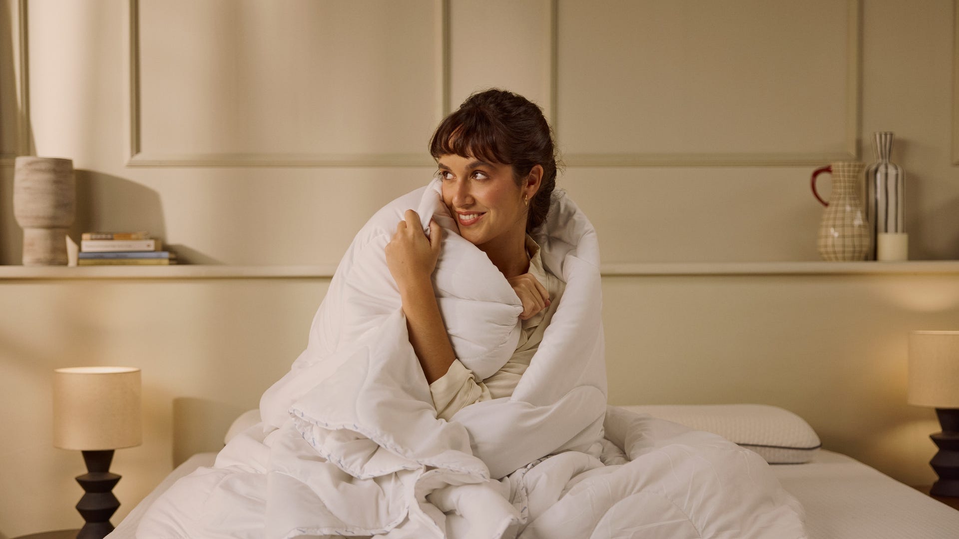 Imagem de uma mulher sentada numa cama, enrolada num edredon Emma Ligeiro