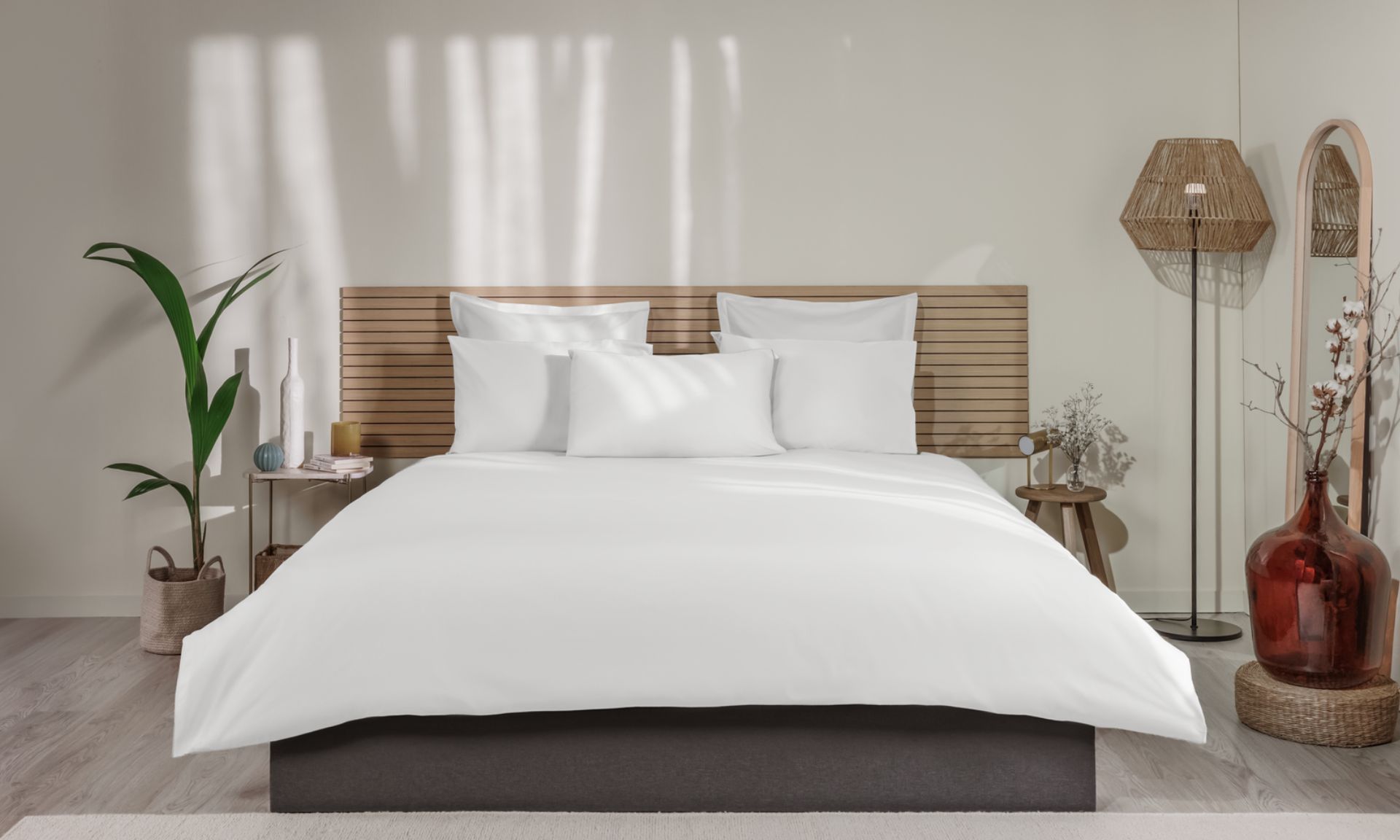 Letto ordinato con biancheria bianca, testiera in legno e decorazioni su entrambi i lati.