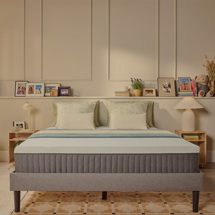 Lit tapissé gris avec matelas blanc, vu depuis le pied du lit.