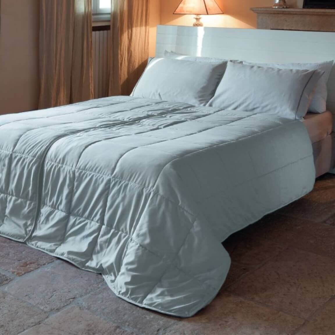 Letto con biancheria bianca in camera accogliente, con comodino, lampada, camino e luce naturale.