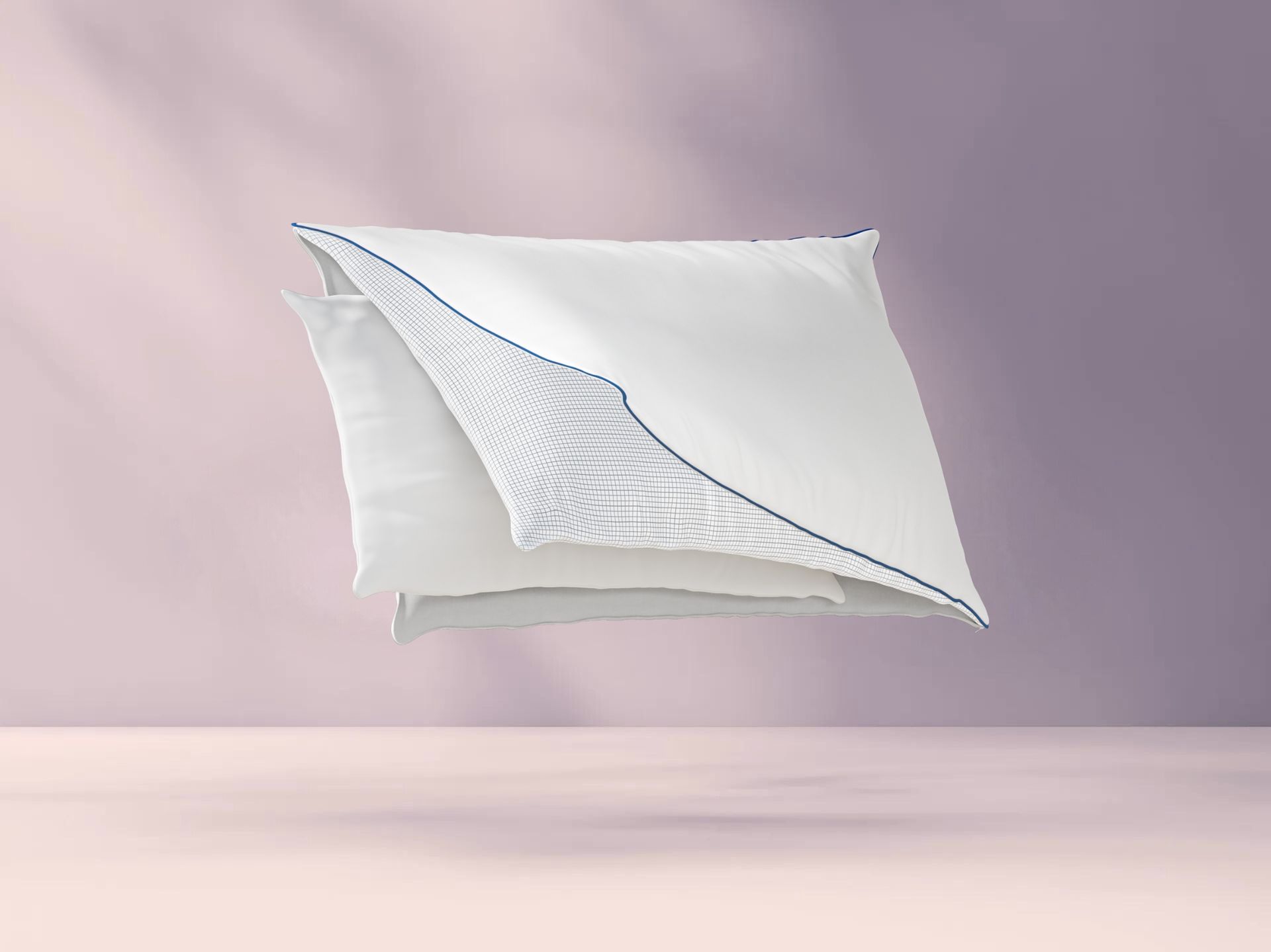 Drie lagen van het Original Cooling Comfort Kussen: witte buitenlaag met blauwe bies, middenlaag met rasterpatroon, en gladde witte binnenlaag; lagen zweven los van elkaar tegen pastelroze achtergrond.