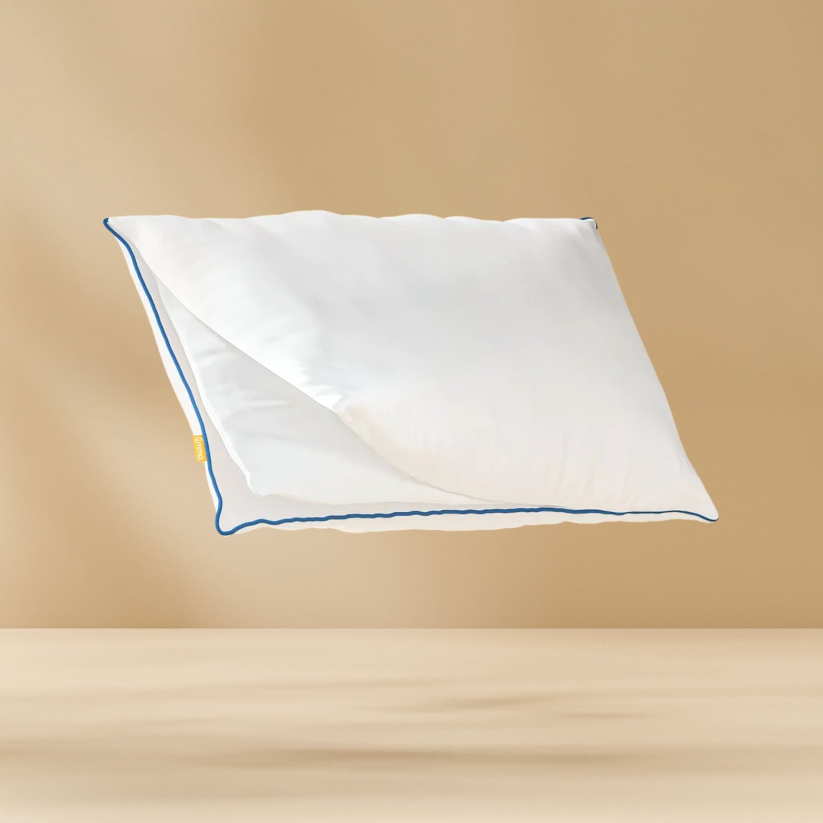 Original Comfort Kussen met witte hoes en blauwe bies zwevend tegen een beige achtergrond, met zichtbaar geel merklabel aan de zijkant.