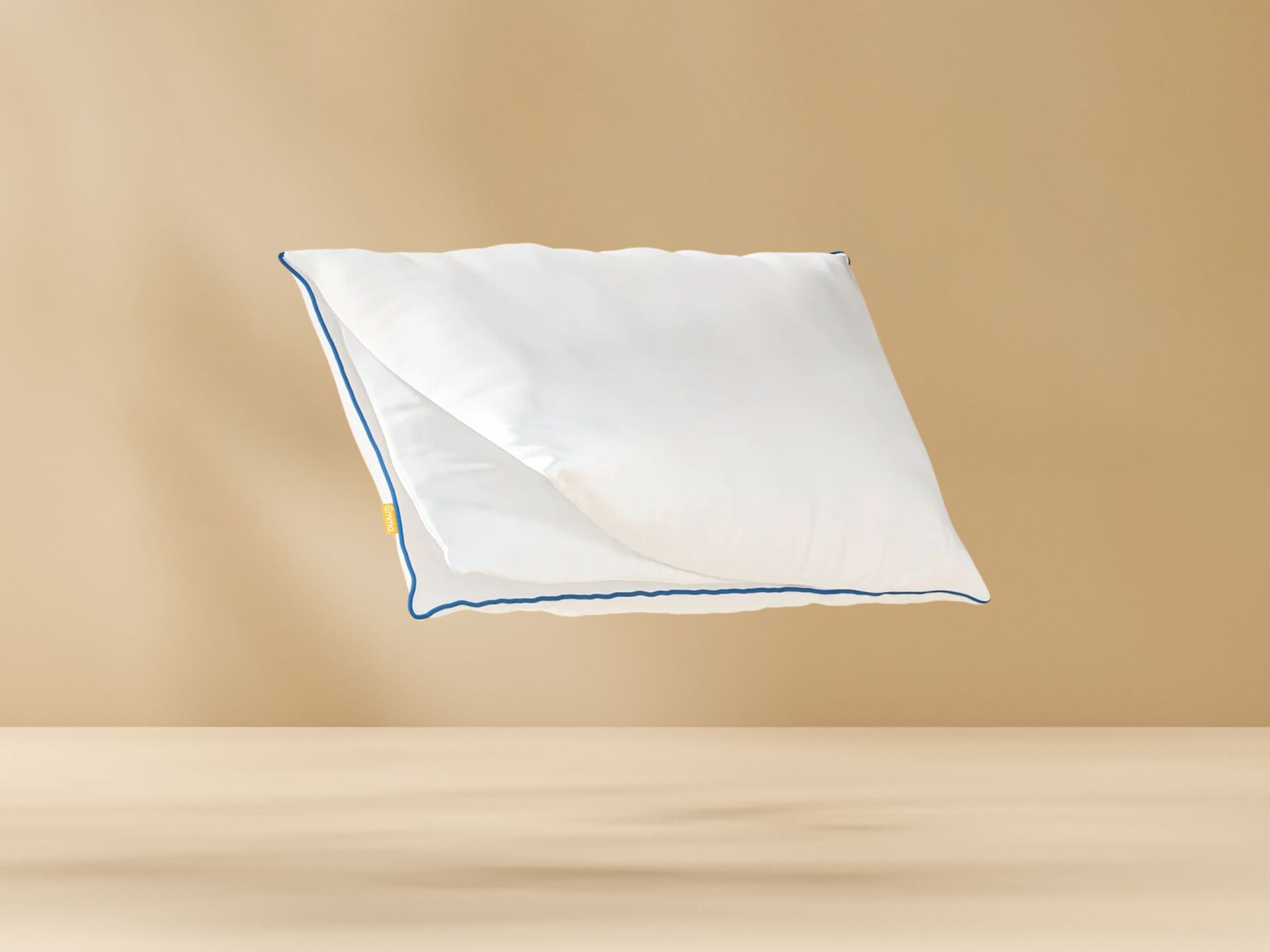 Original Comfort Kussen met witte hoes en blauwe bies zwevend tegen een beige achtergrond, met zichtbaar geel merklabel aan de zijkant.