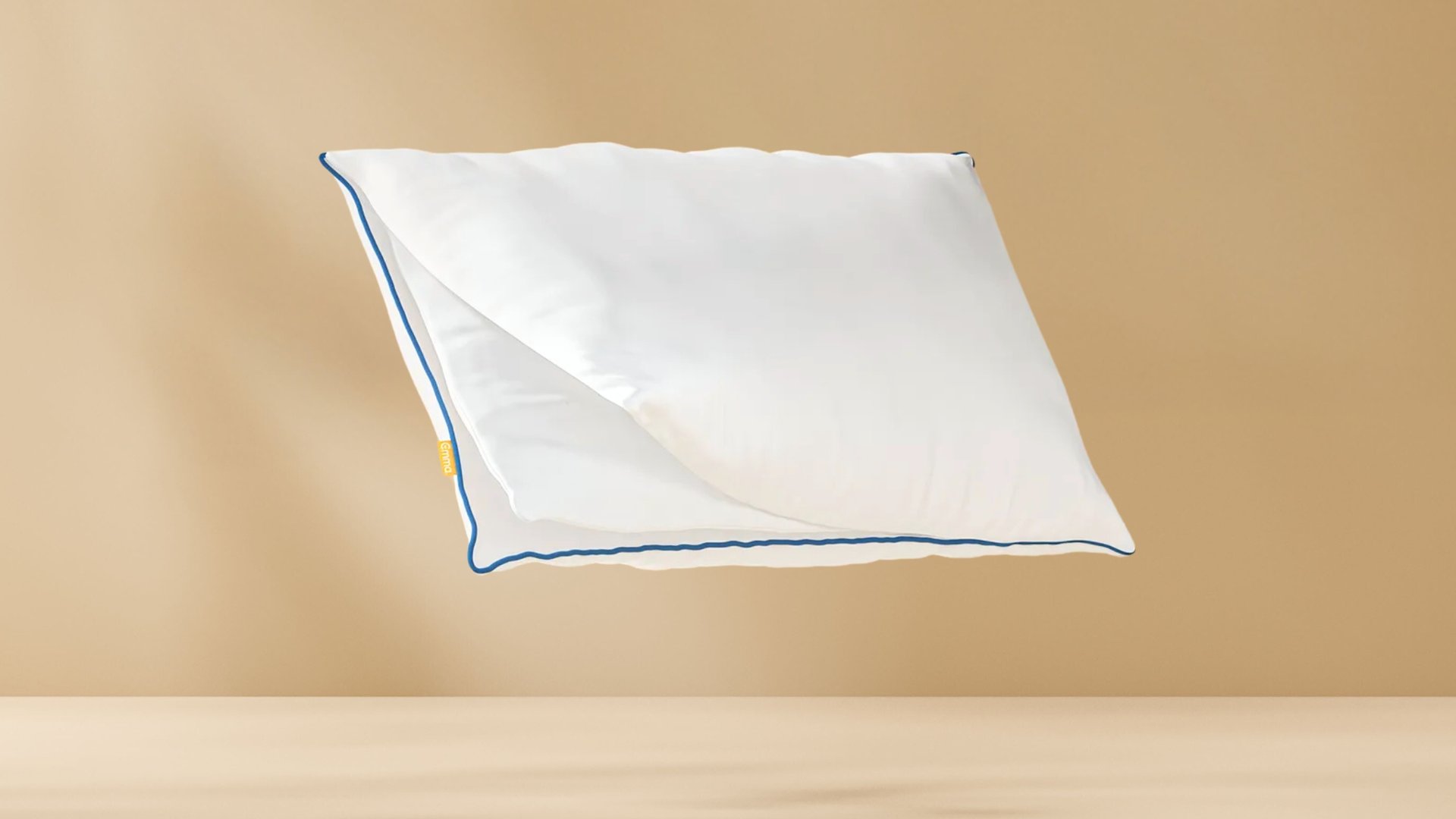 Original Comfort Kussen met witte hoes en blauwe bies zwevend tegen een beige achtergrond, met zichtbaar geel merklabel aan de zijkant.
