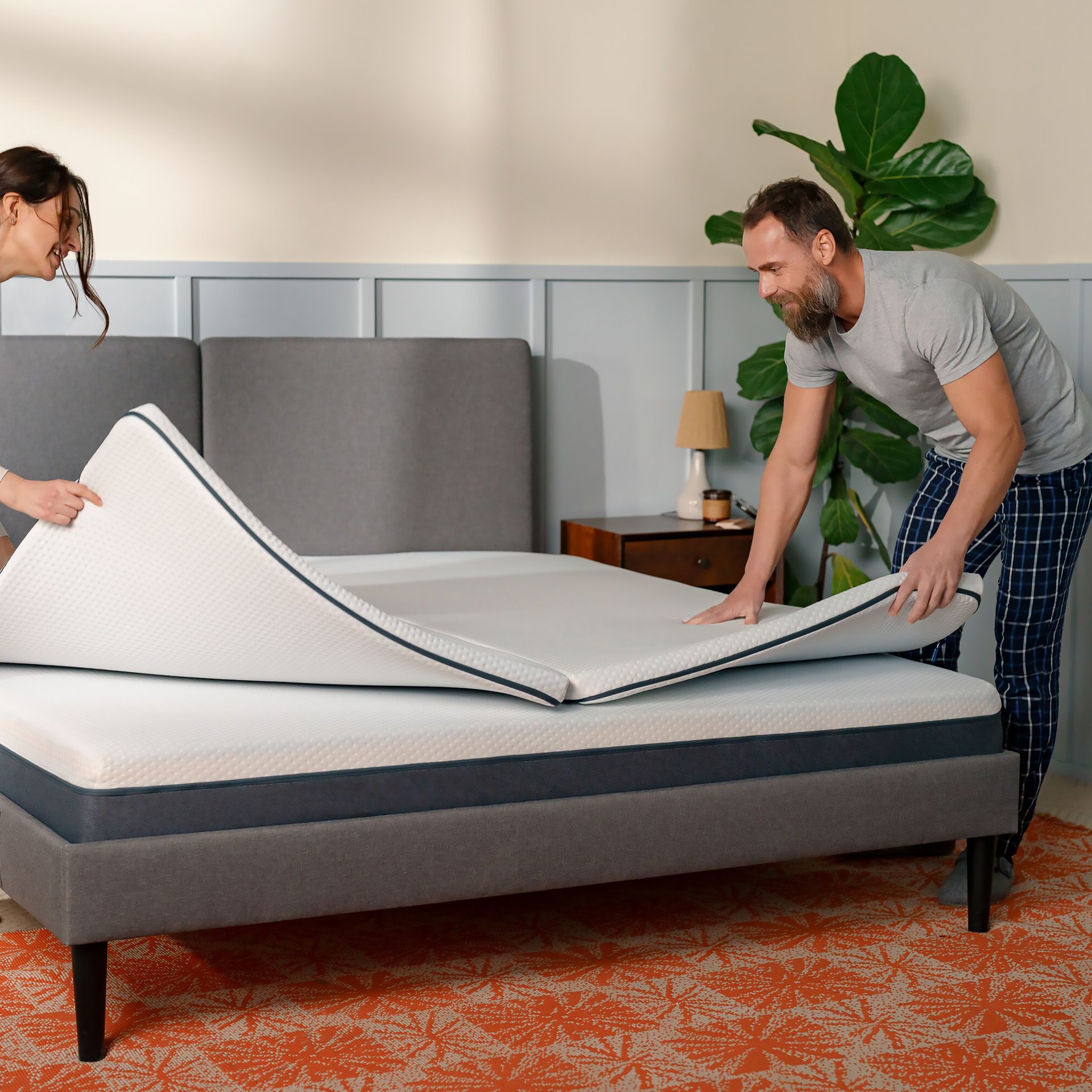 A man and a women placing a topper on top of a mattress.
