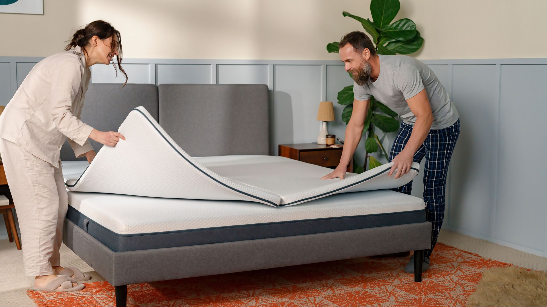 A man and a women placing a topper on top of a mattress.
