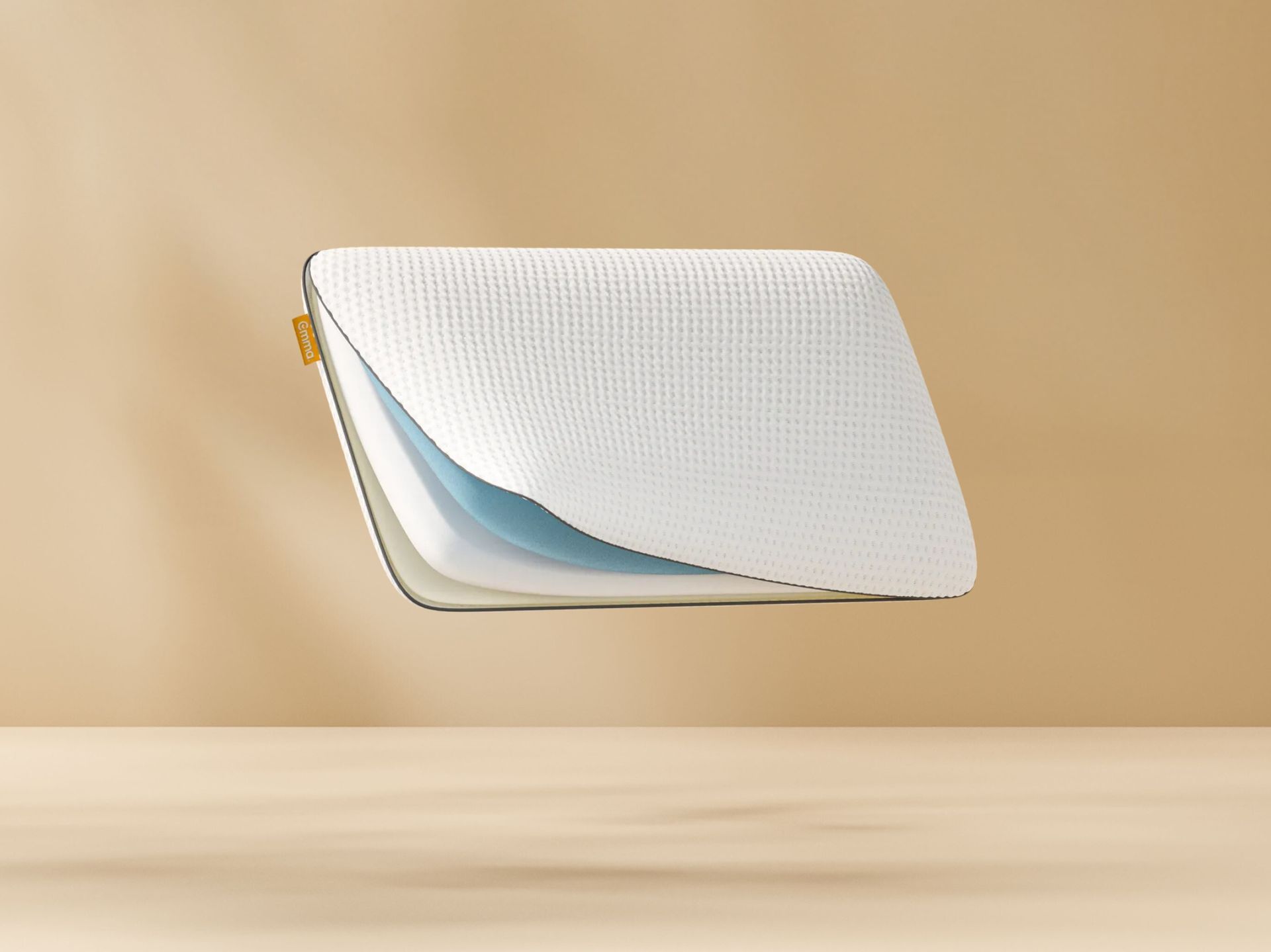 Doorsnede van wit Original Adapt Kussen met geribbeld oppervlak en drie zichtbare lagen (blauw, wit, beige) tegen een beige achtergrond; geel merklabel zichtbaar aan zijkant.