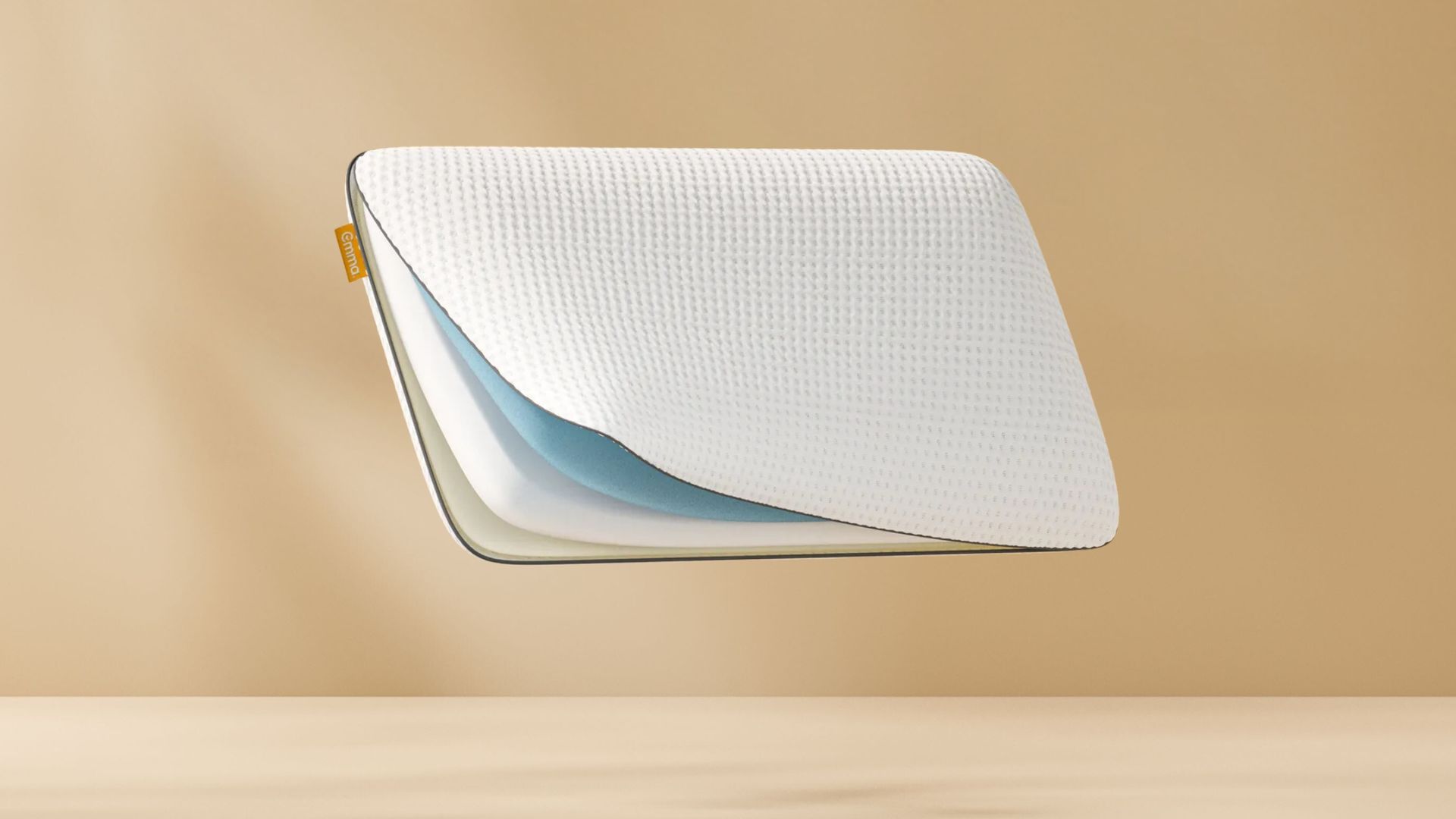 Doorsnede van wit Original Adapt Kussen met geribbeld oppervlak en drie zichtbare lagen (blauw, wit, beige) tegen een beige achtergrond; geel merklabel zichtbaar aan zijkant.