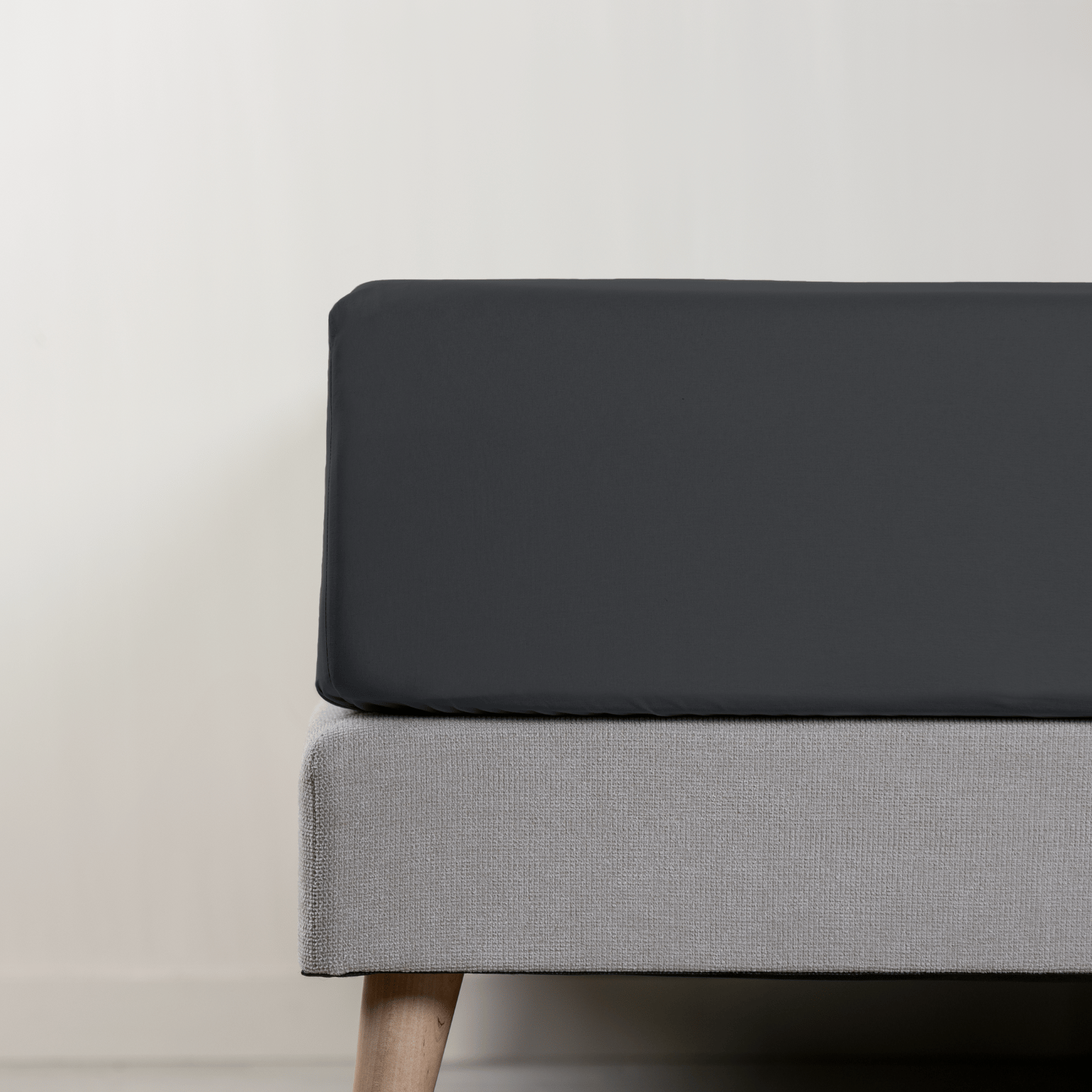 Uma imagem de um lençol de baixo em percal, em cinzento escuro, sob um colchão com fundo cinzento