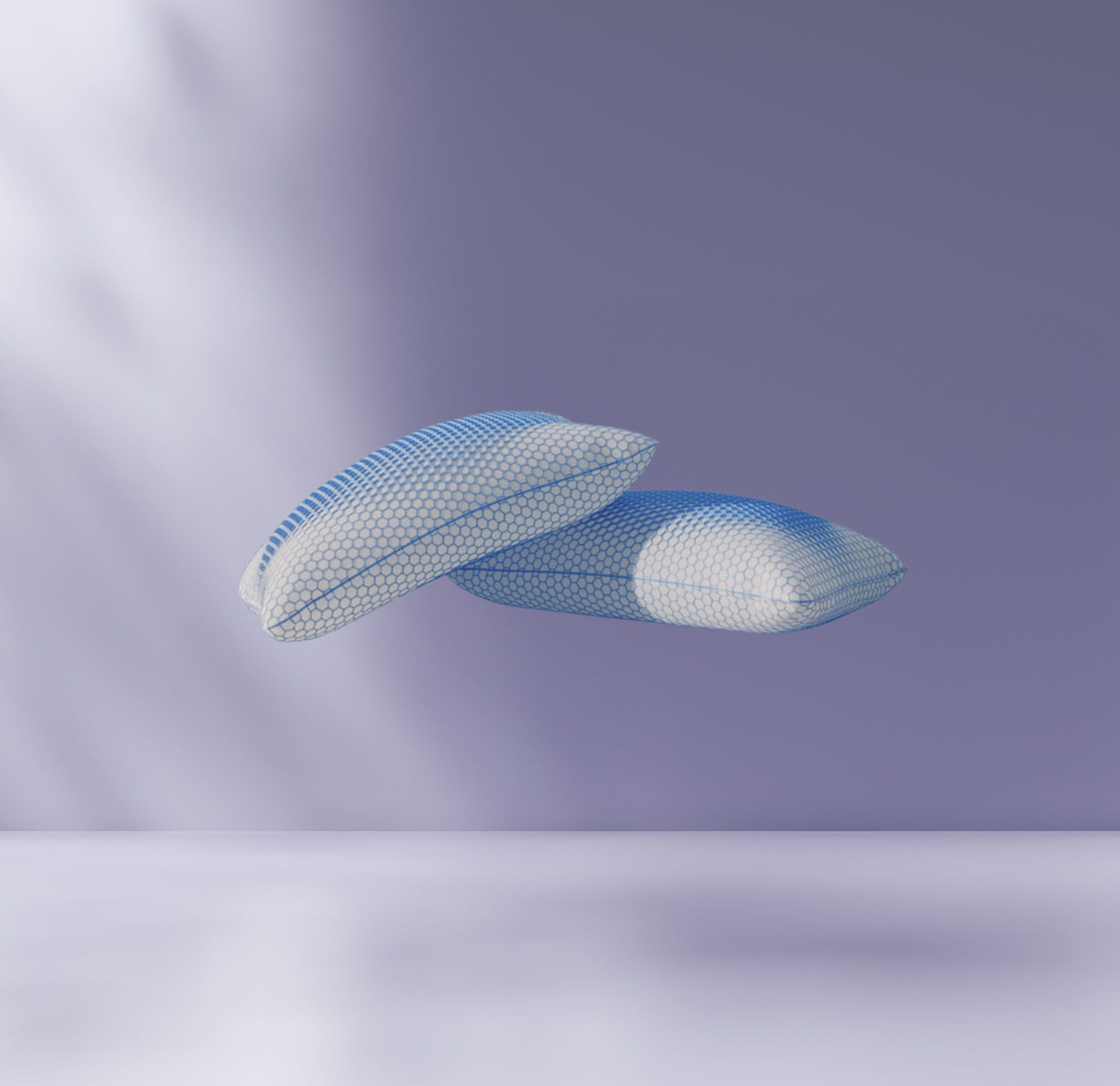 Deux oreillers en maille flottent au-dessus d'une surface lisse et vide, sur un fond violet doux et une lumière naturelle diffuse créant des ombres.