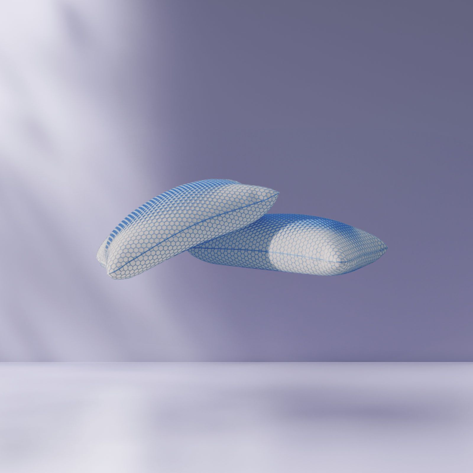 Deux oreillers en maille flottent au-dessus d'une surface lisse et vide, sur un fond violet doux et une lumière naturelle diffuse créant des ombres.