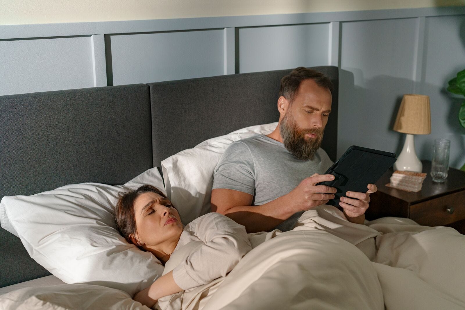 hombre tumbado en la cama mirando la tableta con una mujer al lado