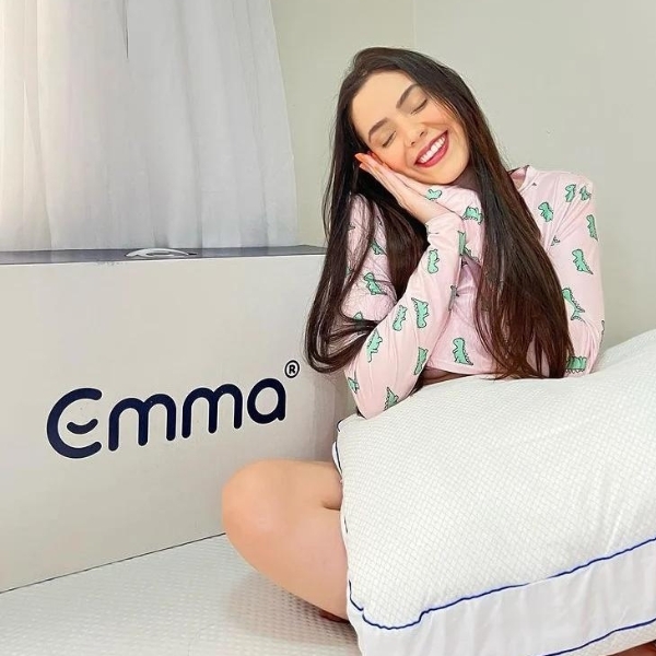 Moça sentada na cama com travesseiro Antiestresse Emma e caixa desse mesmo travesseiro. 