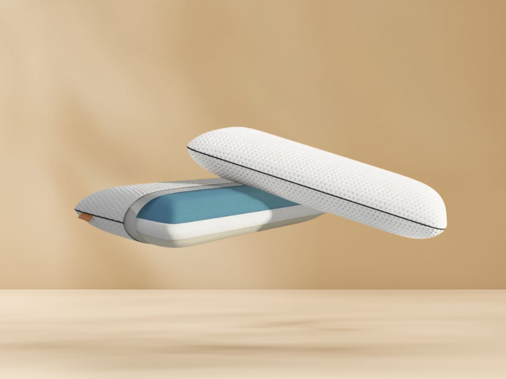 Twee witte Emma kussens met zwarte rits en blauwe binnenlaag zweven tegen beige achtergrond boven houten ondergrond; één kussen deels geopend, toont binnenstructuur van schuim.