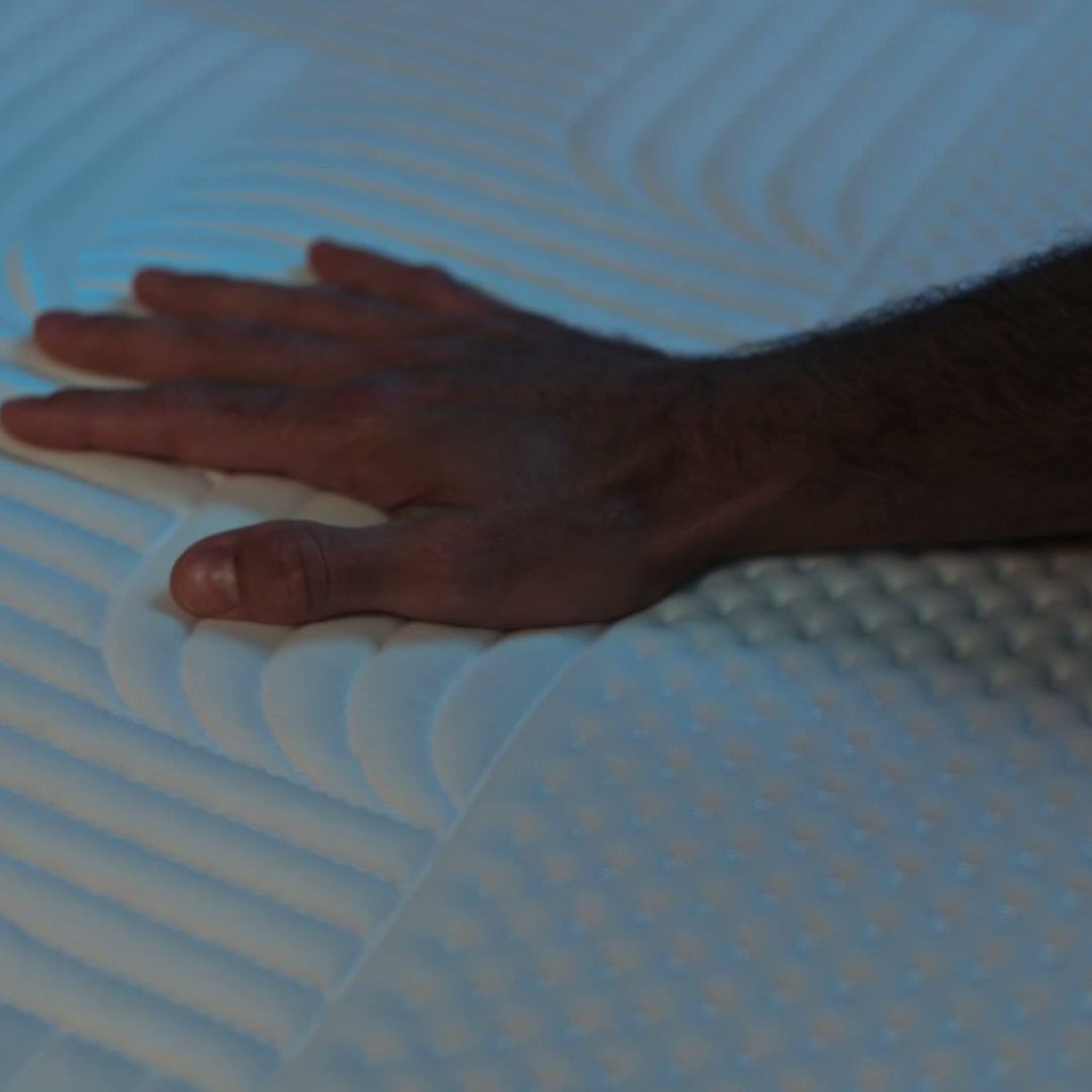 Hand touching Emma Performance Topper surface showing quilted texture detail under blue lighting.