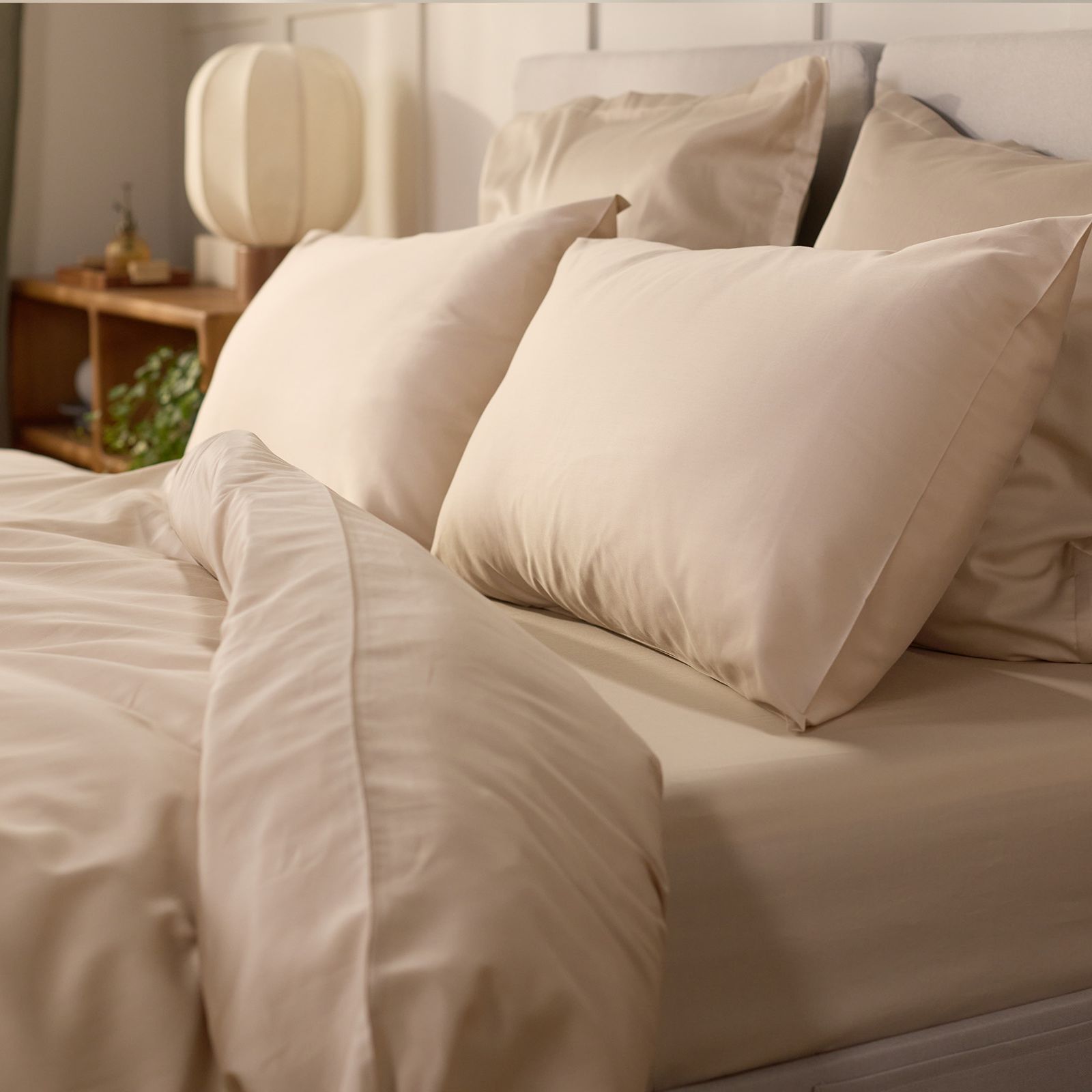 Beige cotton bedding set with matching pillowcases styled on a light grey upholstered bed.