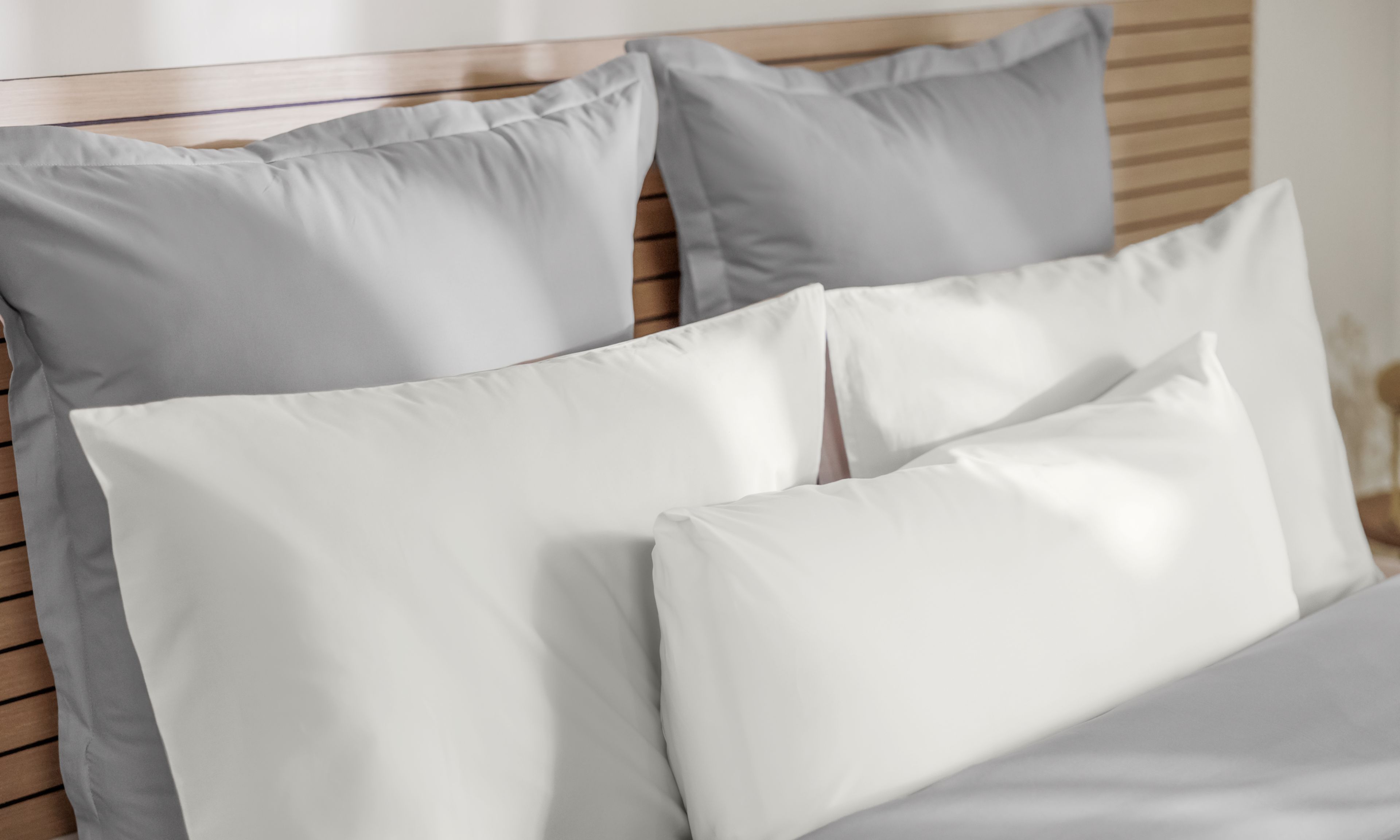 Letto ordinato con testiera in legno, cuscini grigi e bianchi disposti in tre file.