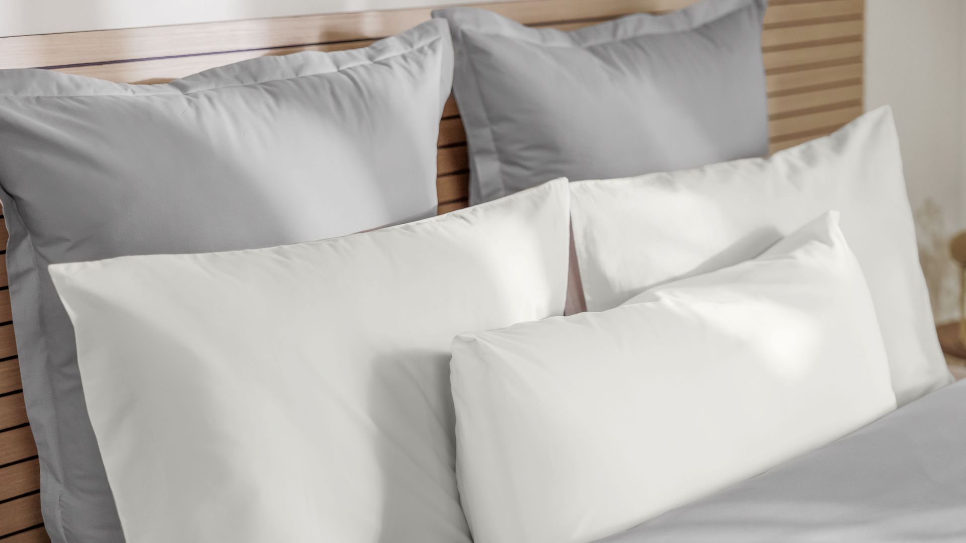 Letto ordinato con testiera in legno, cuscini grigi e bianchi disposti in tre file.