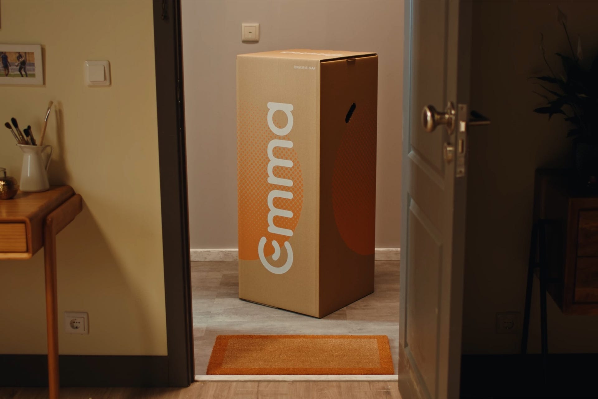 Emma Box steht hinter geöffneter Wohnungstür auf Fußmatte im Flur