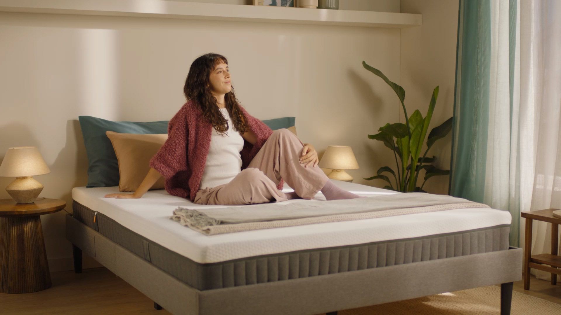 Person sitting on a grey upholstered bed with a hybrid mattress demonstrating everyday use.