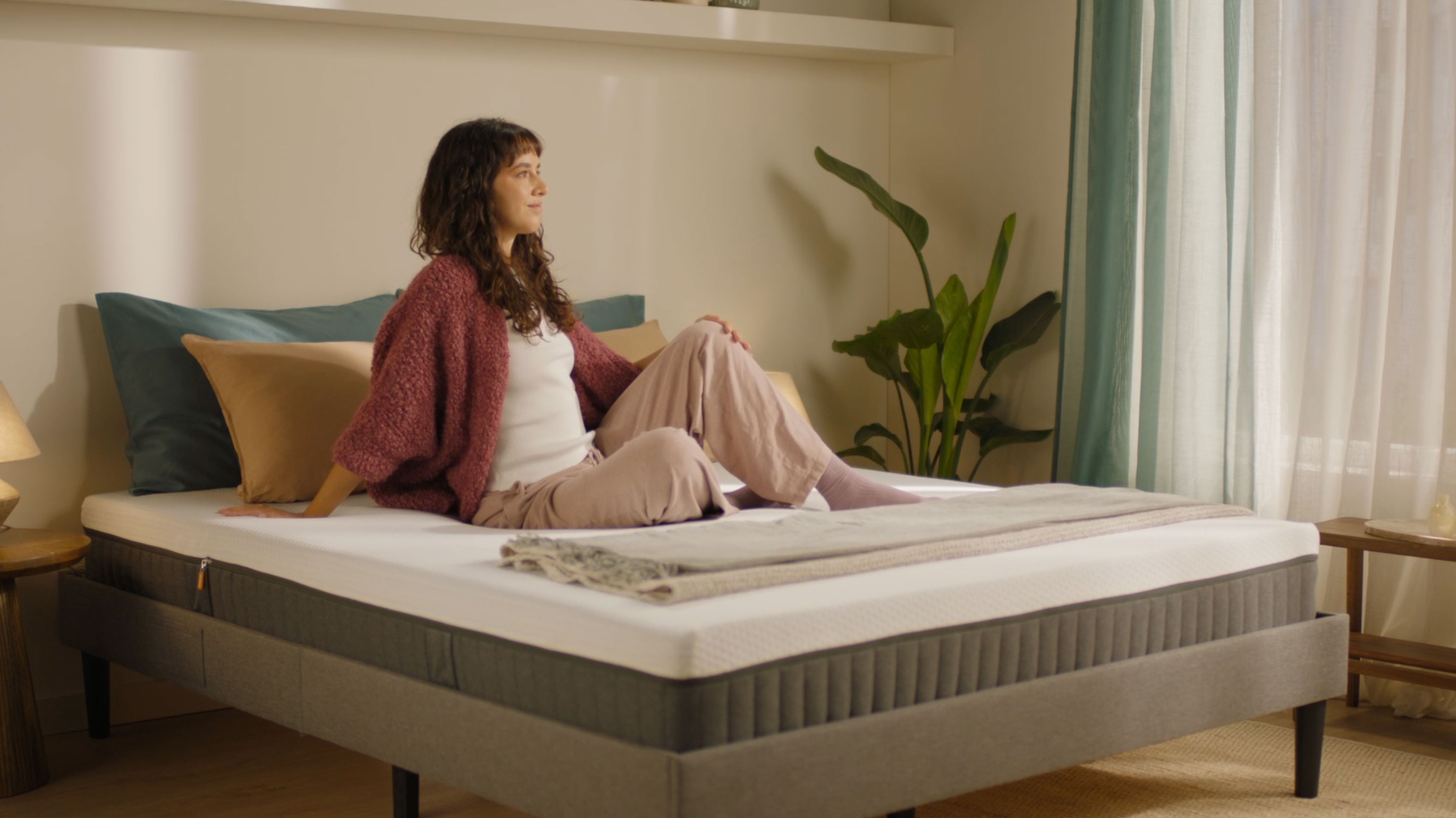 Person sitting on a grey upholstered bed with a hybrid mattress demonstrating everyday use.