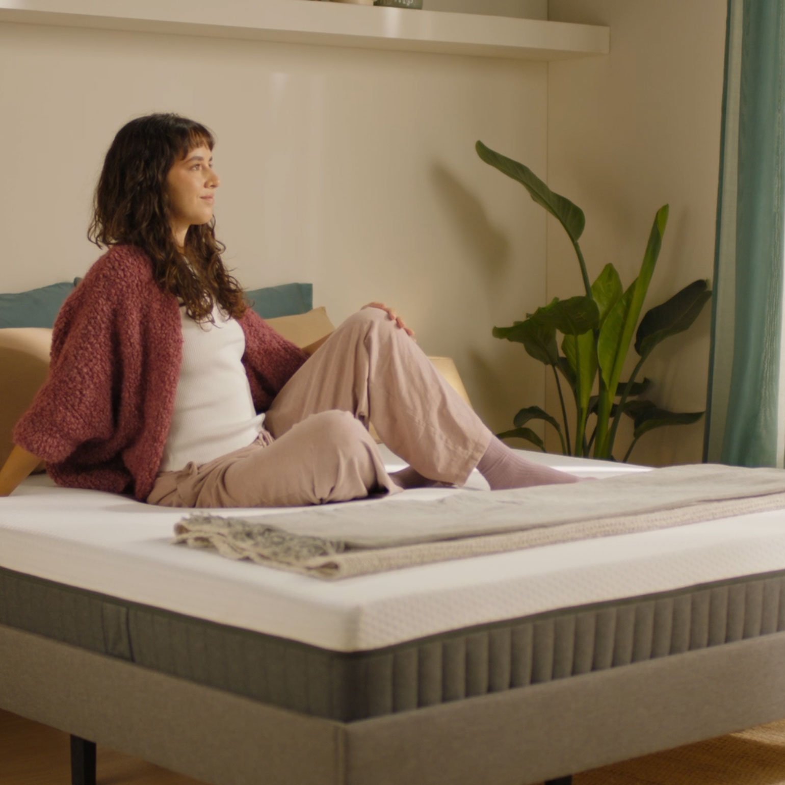 Person sitting on a grey upholstered bed with a hybrid mattress demonstrating everyday use.