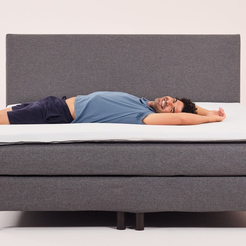 A man and a women placing a topper on top of a mattress.