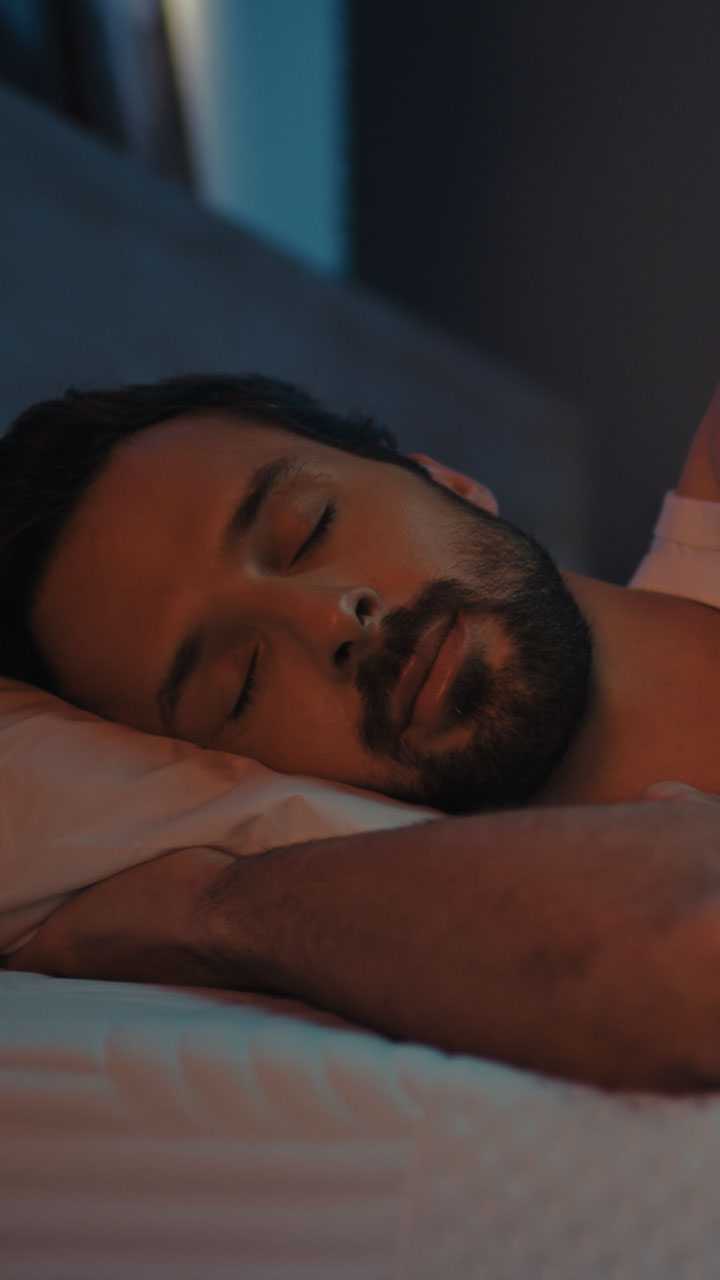 Man sleeping on Emma mattress with head supported on pillow in low light.