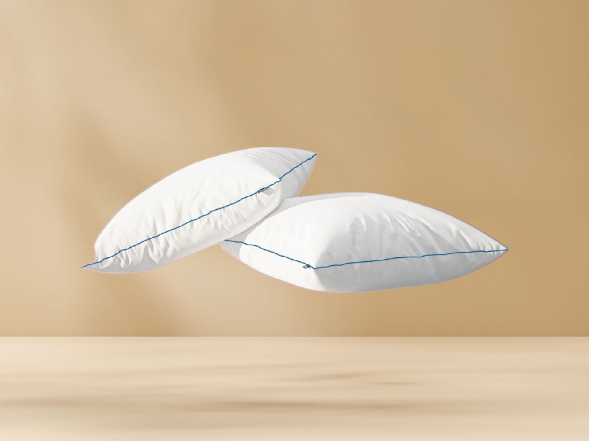 Twee witte Original Comfort Kussens met blauwe bies zweven tegen beige achtergrond; benadrukt setverpakking, luchtige uitstraling en strakke productpresentatie.