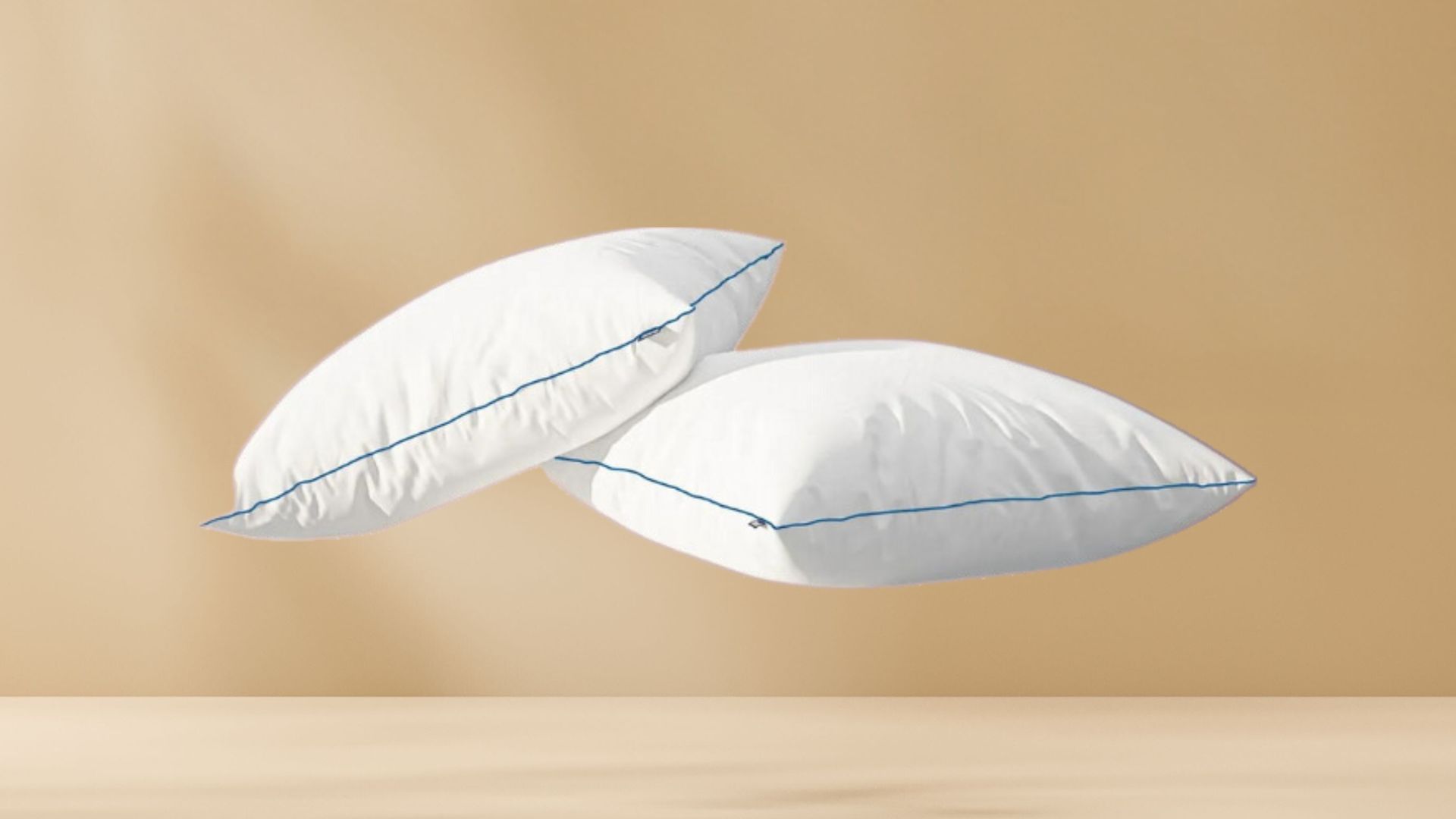 Twee witte Original Comfort Kussens met blauwe bies zweven tegen beige achtergrond; benadrukt setverpakking, luchtige uitstraling en strakke productpresentatie.