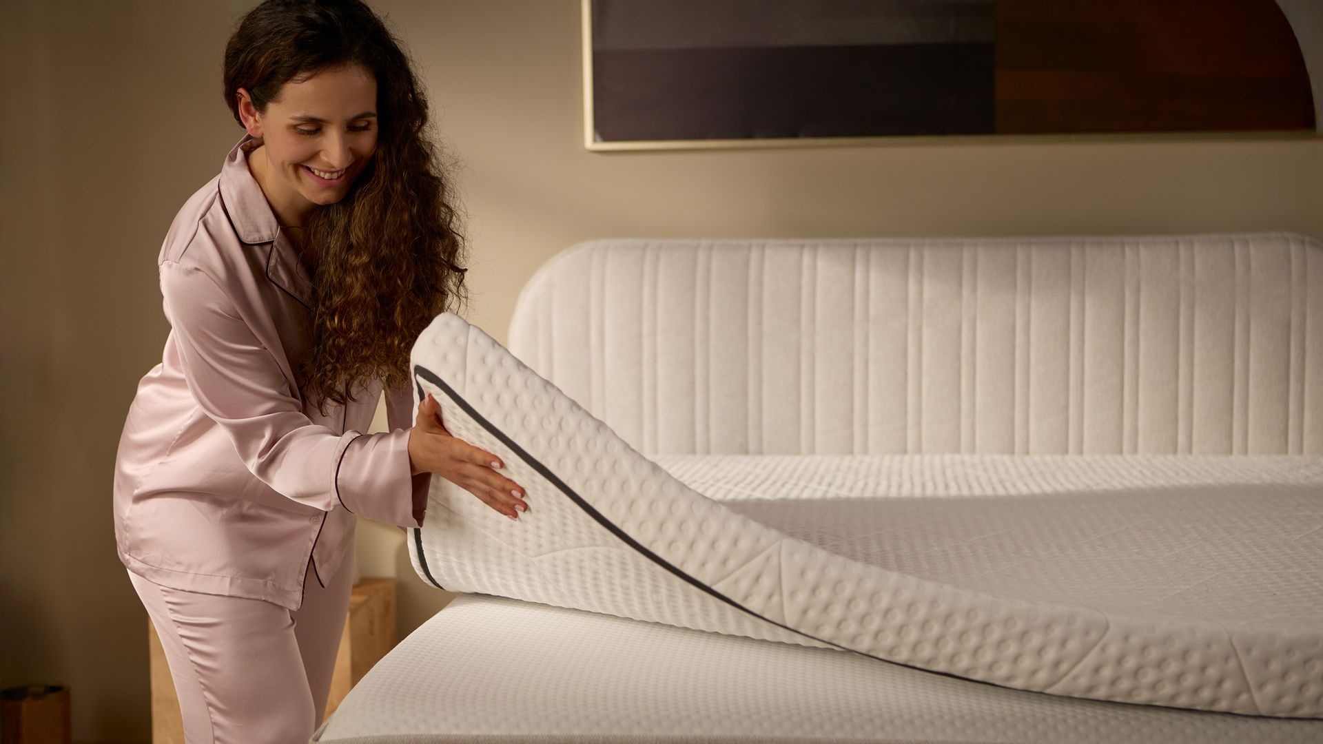 Detailansicht mit einer Person, die einen separaten Matratzen-Topper anhebt; zeigt Dicke und flexible Konstruktion.