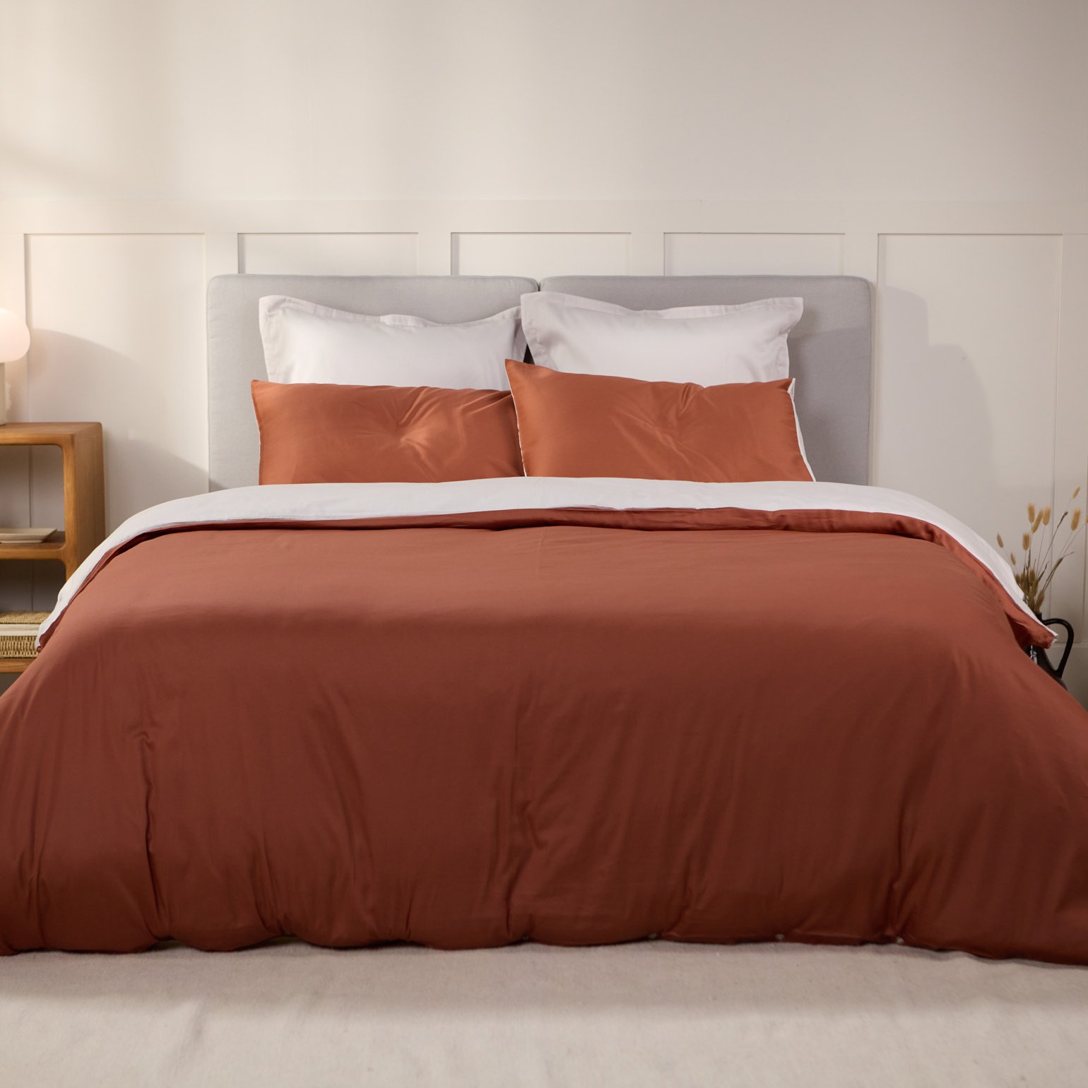 Lit avec une housse de couette terracotta et des oreillers assortis.