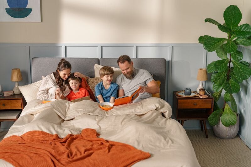 una familia con 2 niós encima de la cama leyendo un cuento infantil
