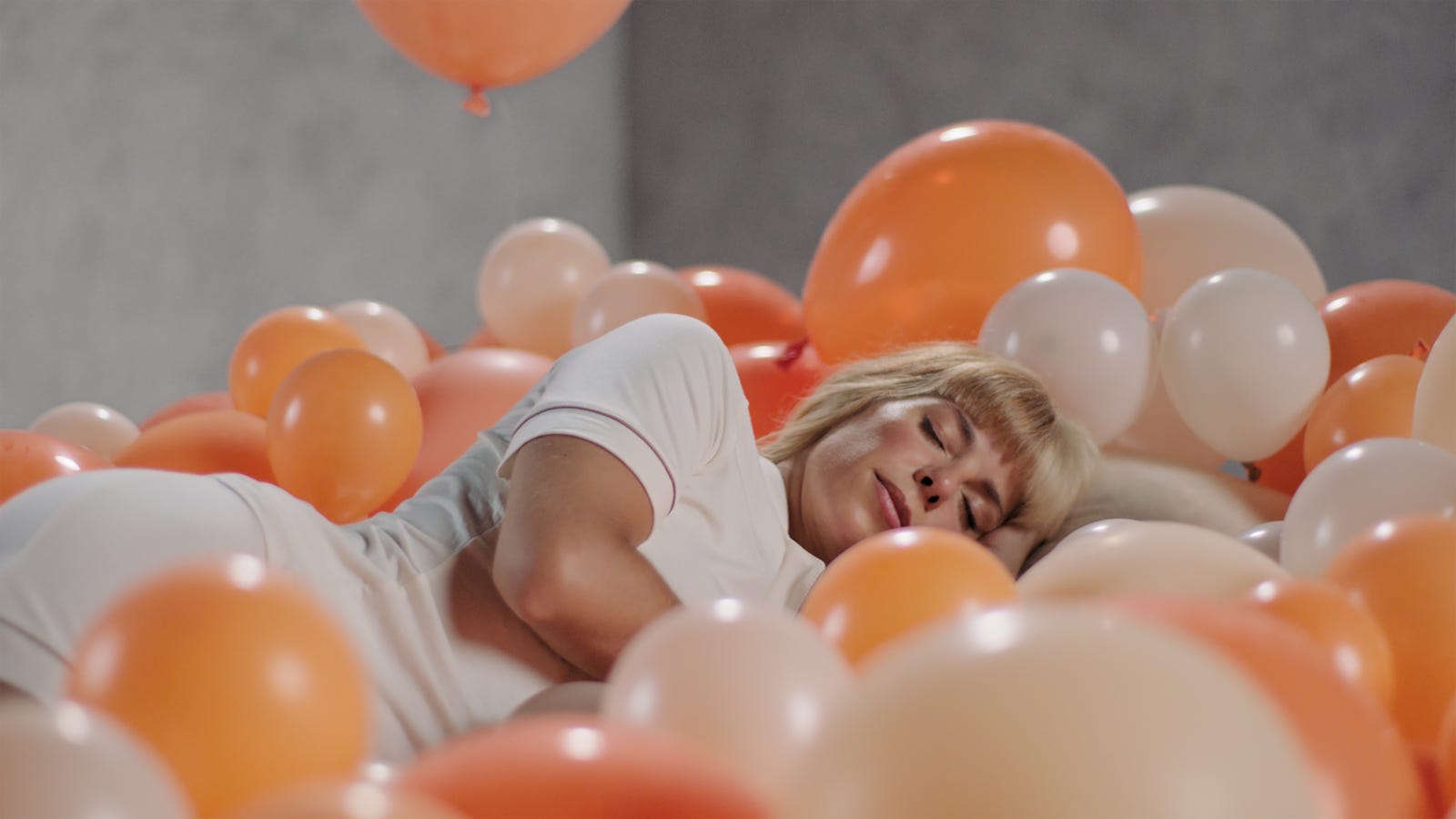 una mujer rubia tumbada en una habitación llena de globos naranjas
