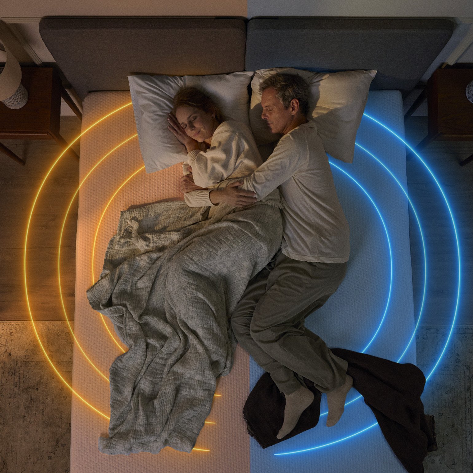 Couple sleeping on a mattress with warm and cool lighting shown on each side.