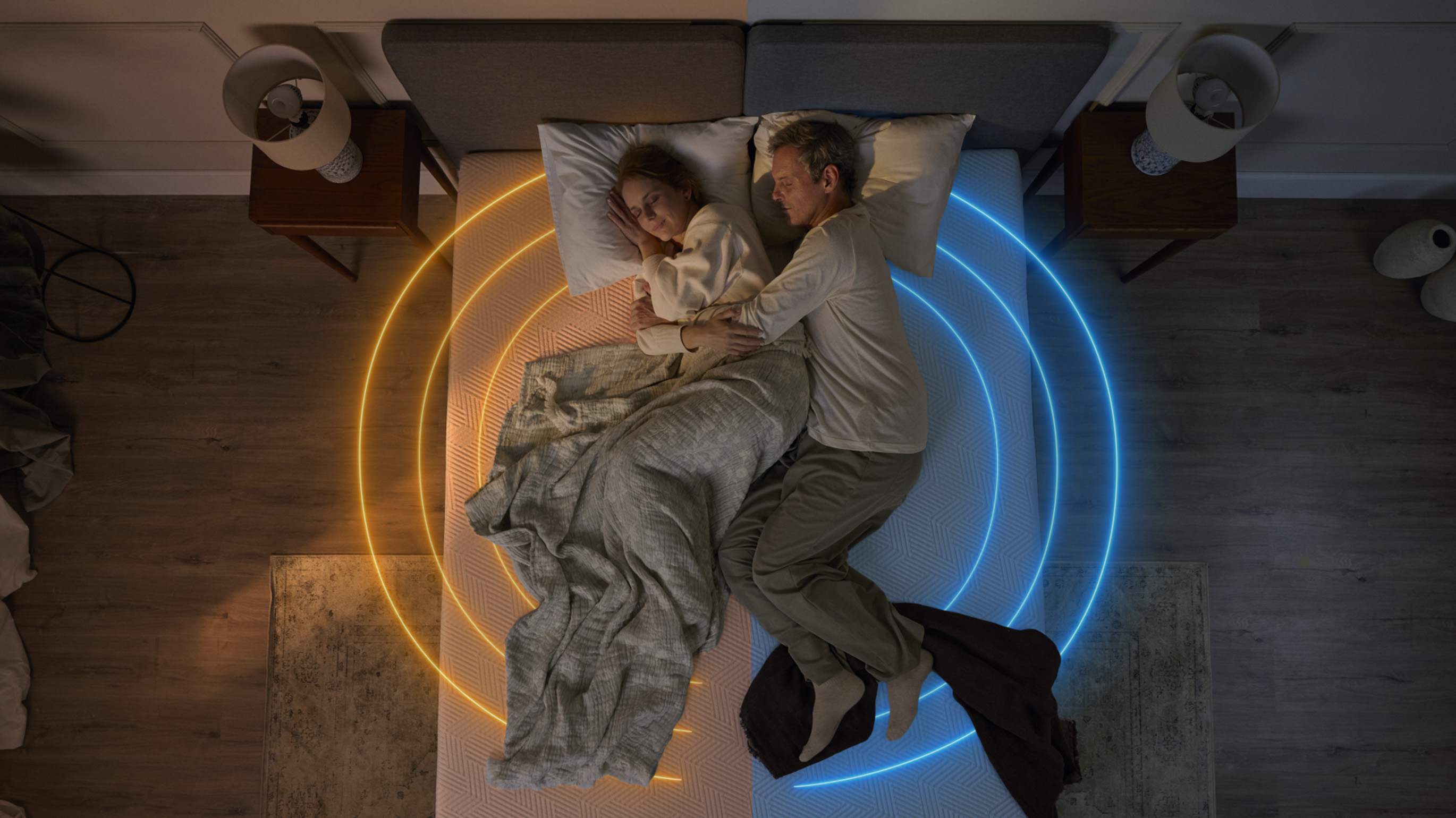 Couple sleeping on a mattress with warm and cool lighting shown on each side.