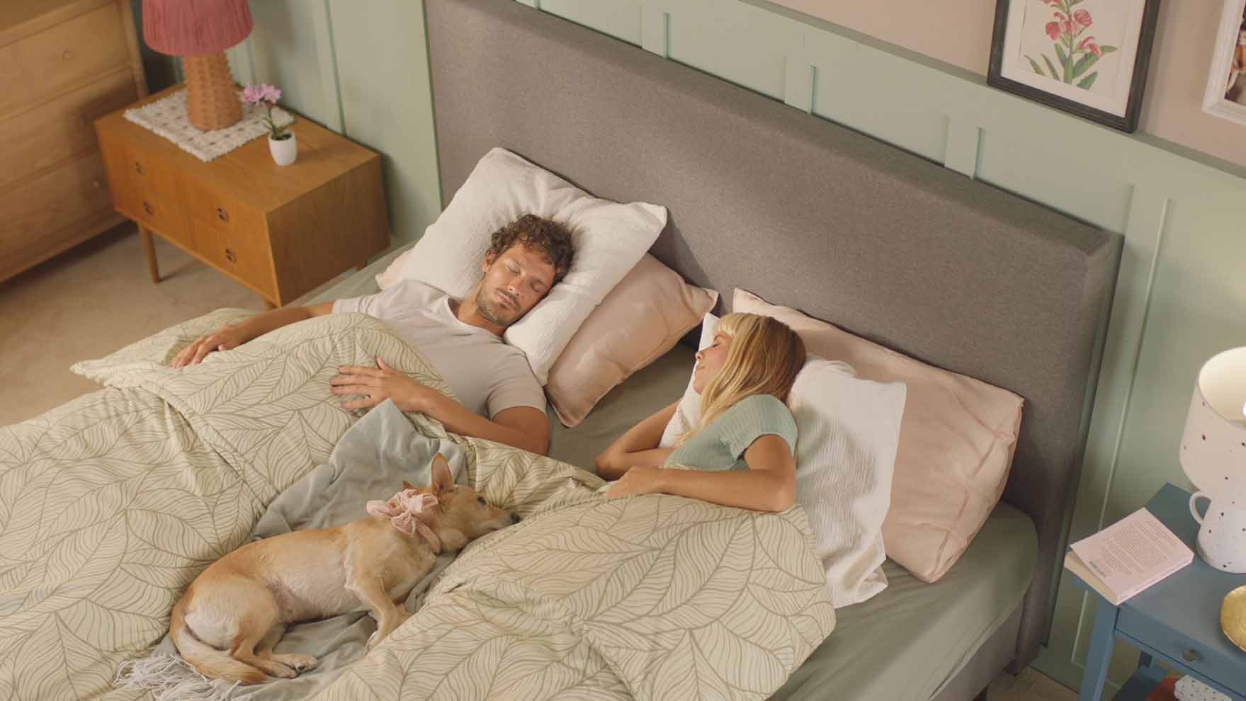 Familie liest gemeinsam im Bett mit beiger Bettwäsche und grauem Kopfteil.