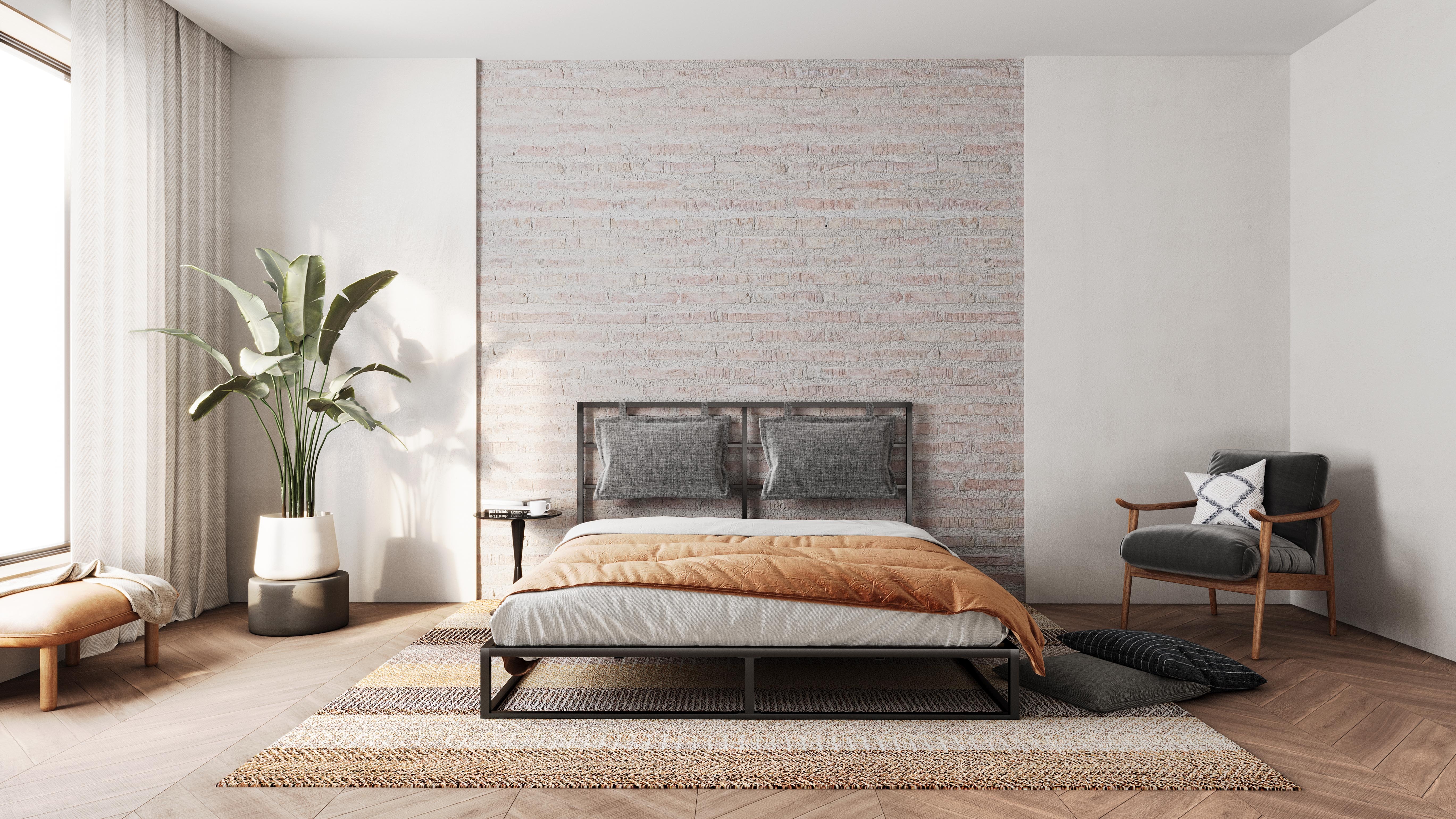 Metallbett mit grauem Kopfteil und oranger Decke vor Backsteinwand